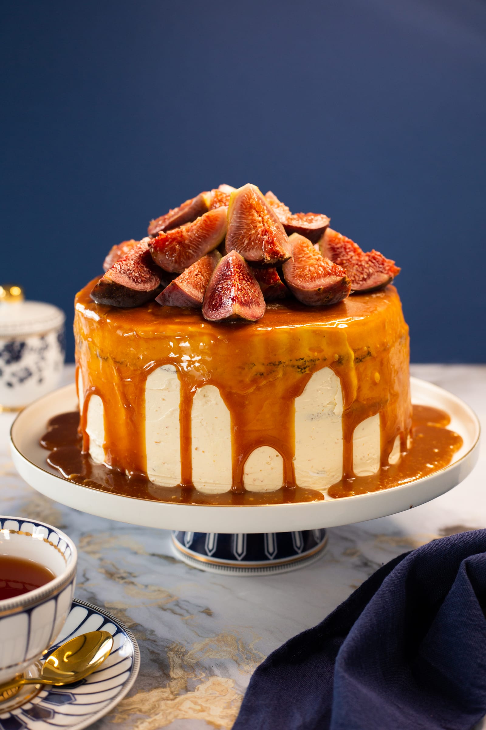 Devil's food cake with hazelnut buttercream on a white stand, dripping caramel and topped with fresh figs