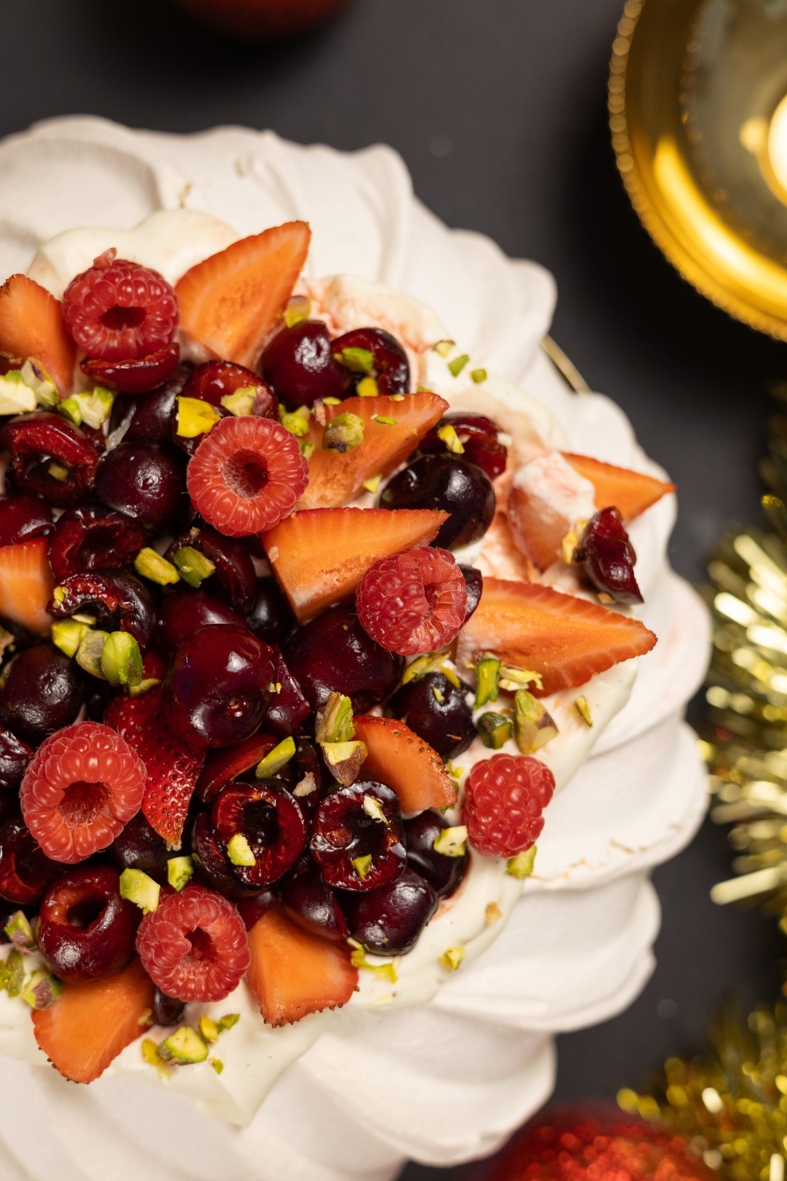 Cherries, raspberries and chopped pistachios on the cream of a very berry pavlova, close up from above