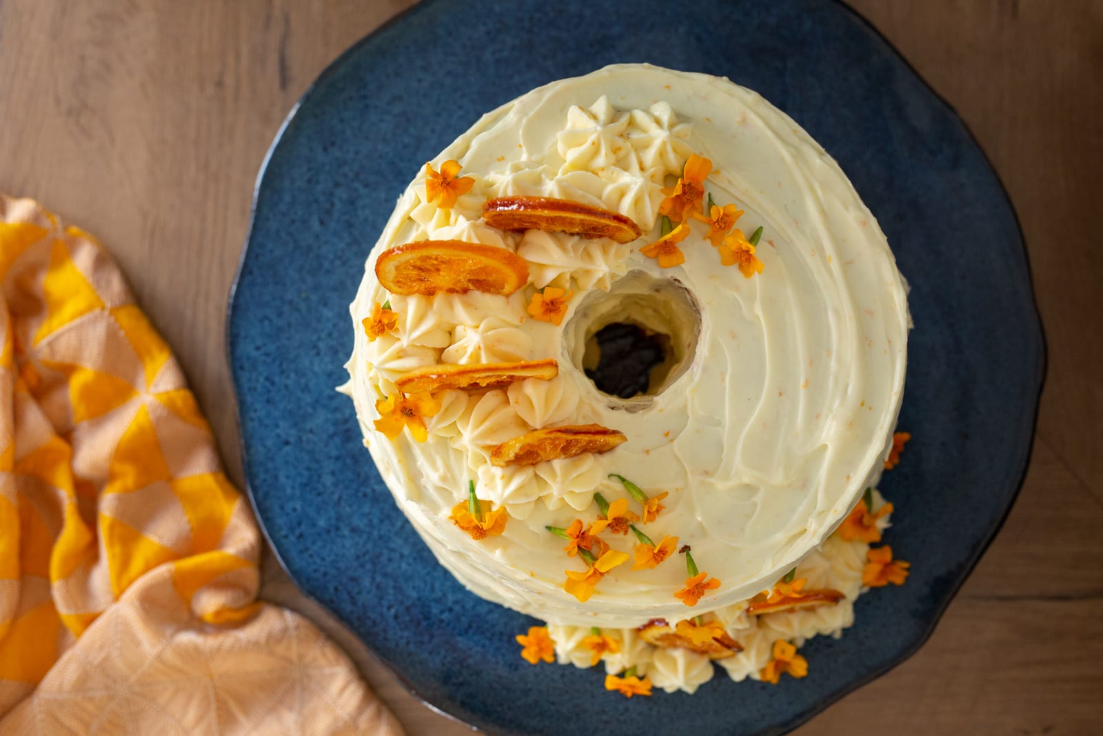 The orange cream chiffon cake on a blue plate from above, ringed with candied oranges and flowers