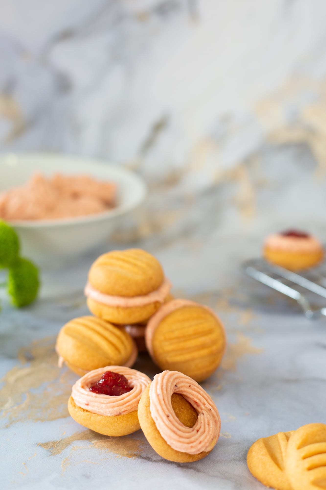 A pile of sandwiched custard and jelly biscuits, the bowl of filling behind