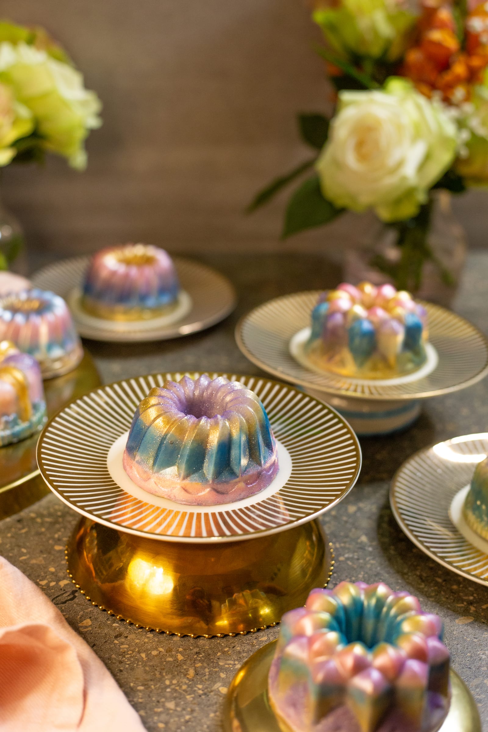 Dubai pistachio burfee bundts on gold stands and plates, with flowers behind