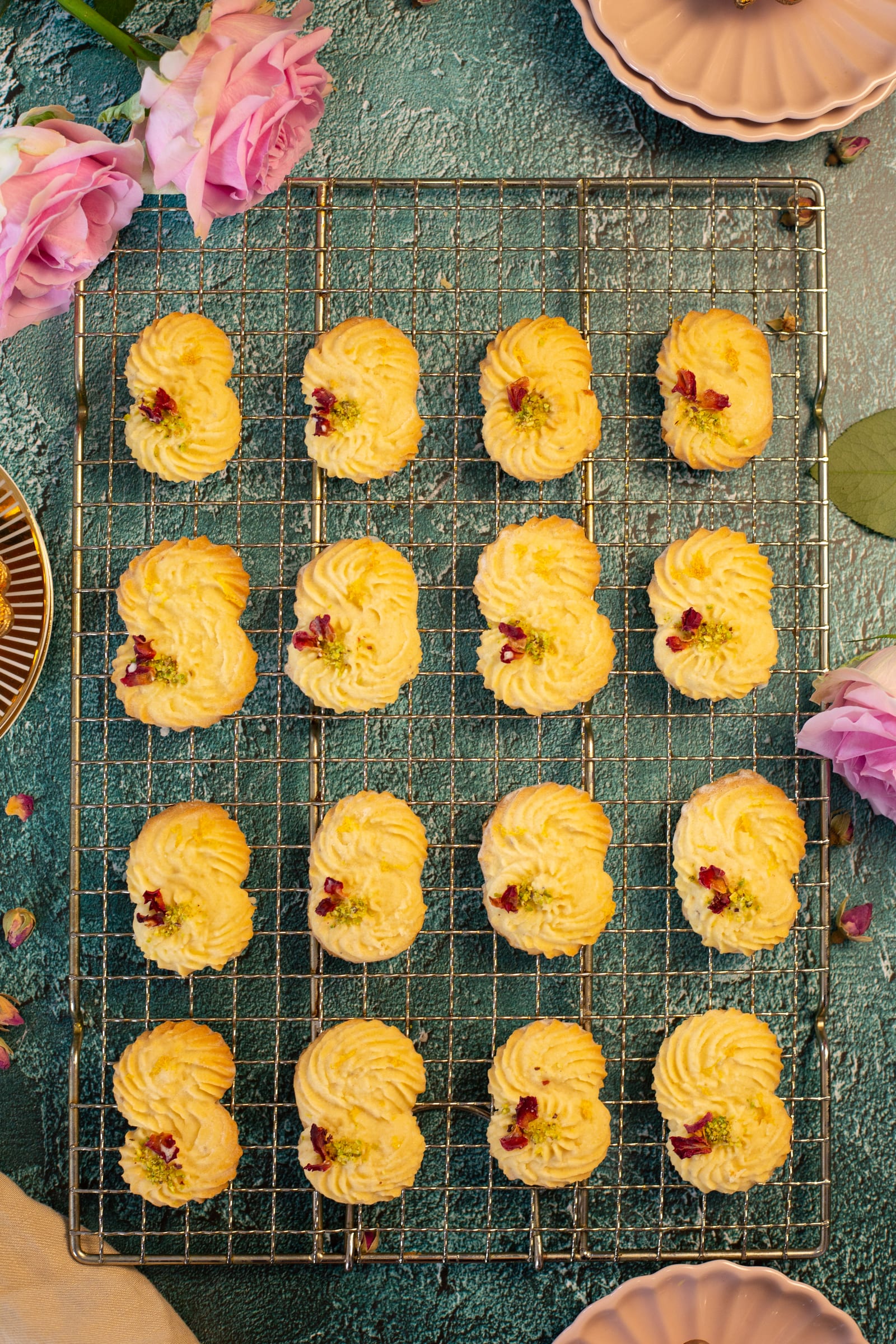 Piped lemon, rose and cardamom biscuits on a wire rack, from above