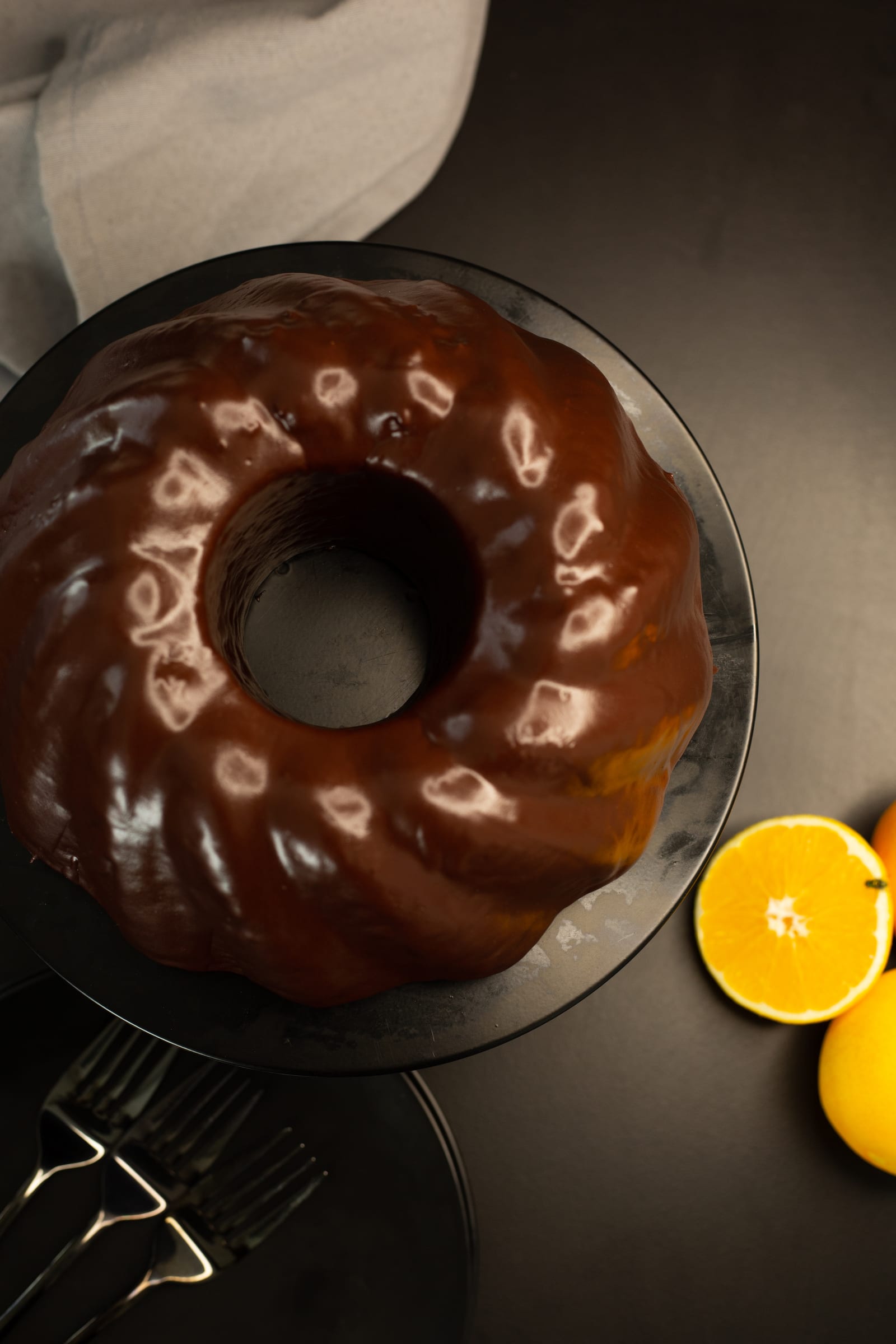 The glazed orange and olive oil bundt from above, on a black plate with orange halves