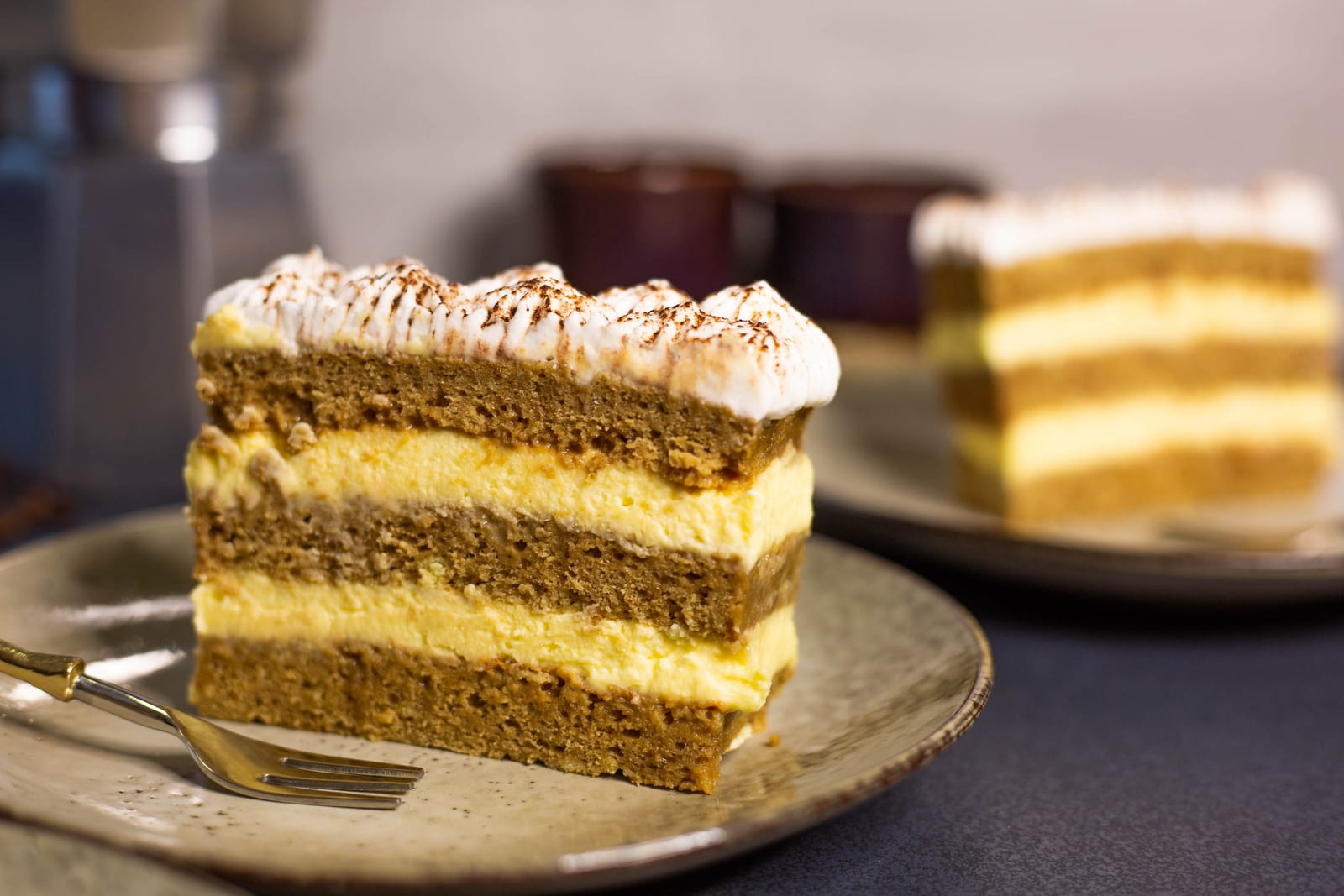 A slice of tiramisu tres leches cake on a plate in front of the rest of the cake