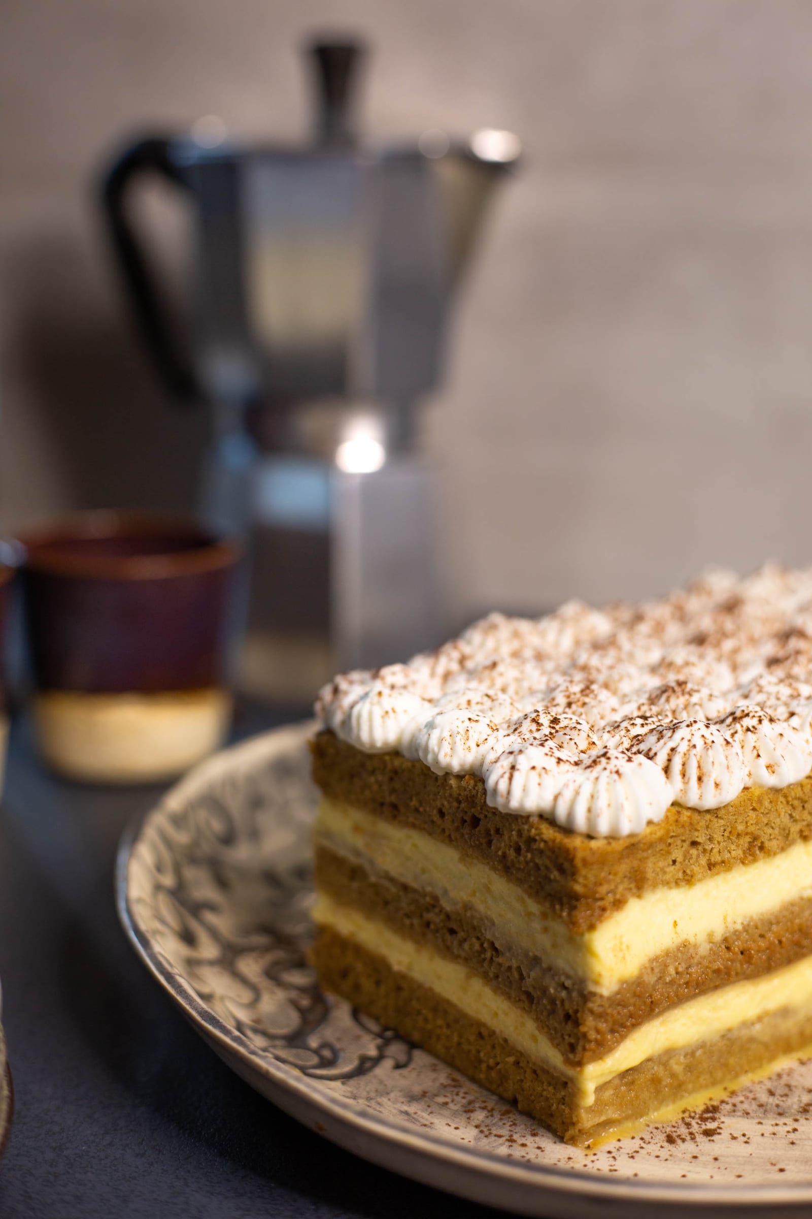 The whole tiramisu tres leches cake on a plate, showing its layers and cocoa-dusted cream