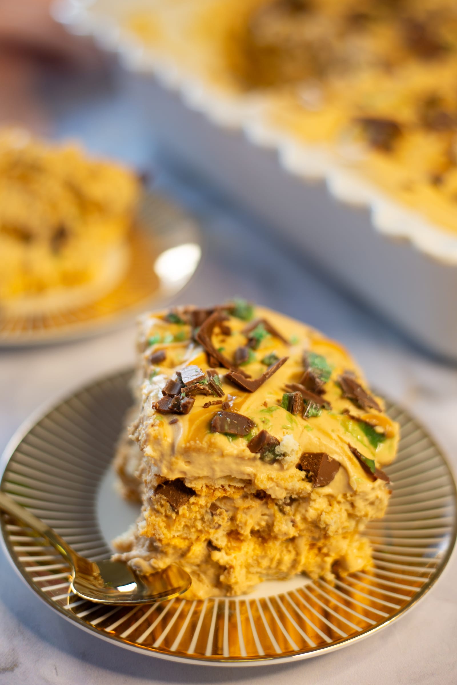 A slice of Peppermint Crisp tart on a gold plate, showing the layers of biscuit and caramel cream