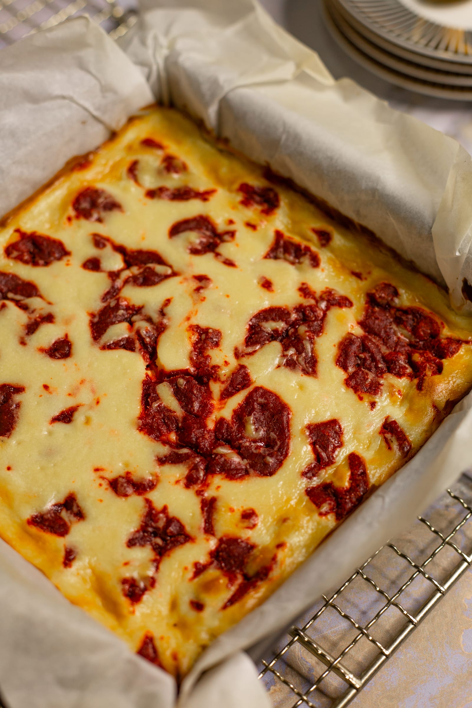 Red velvet cheesecake blondies fresh from the tin in their baking paper, close up at an angle, showing the cream cheese swirl