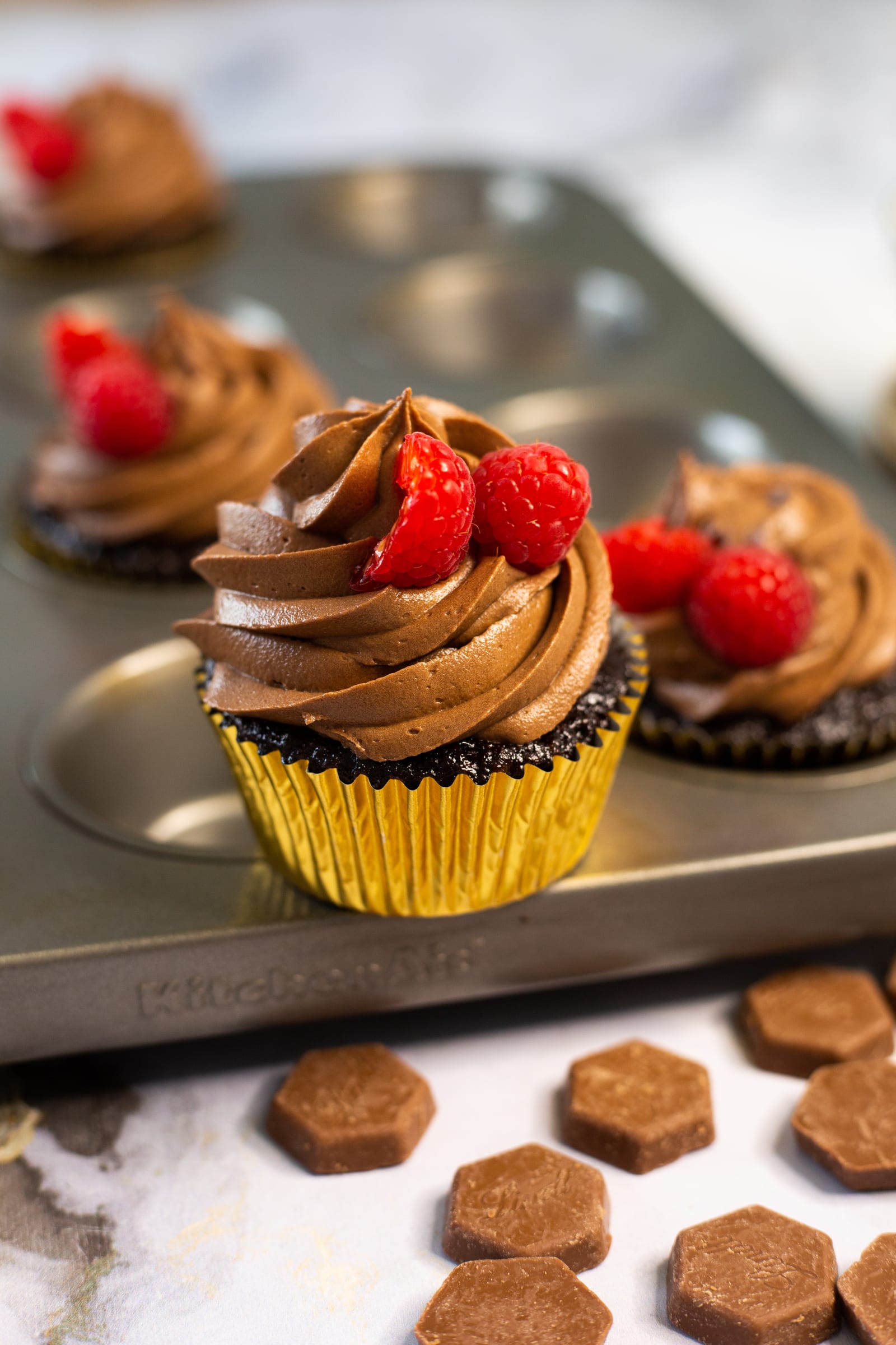 An ultimate triple chocolate cupcake with raspberries in a gold case in front of the tin