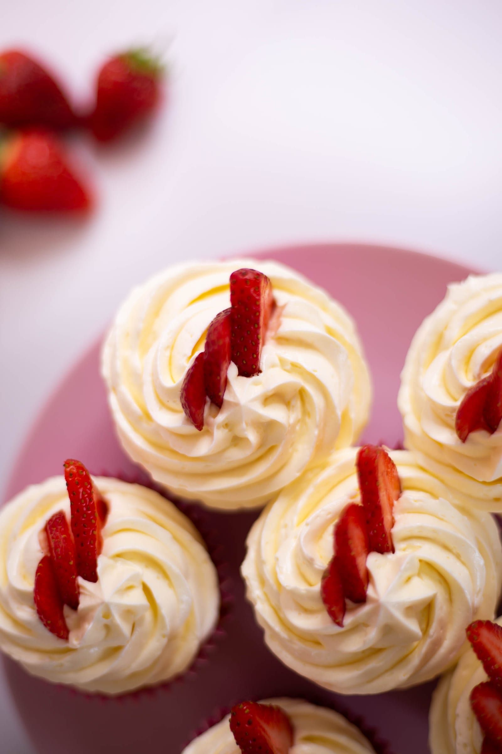 Close-up of the swirled buttercream and strawberries on strawberry and white chocolate cupcakes, from above