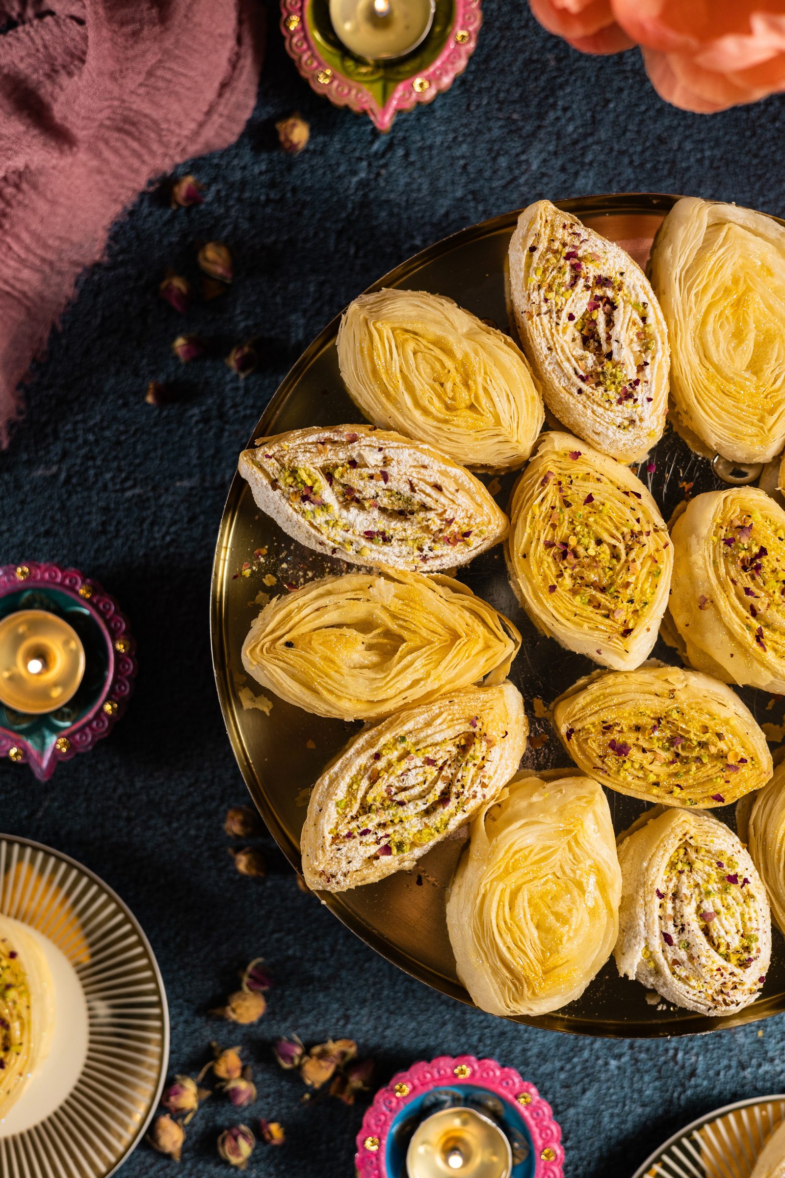 Banana puri on a gold tray with diyas, rosebuds and a pink cloth, from above