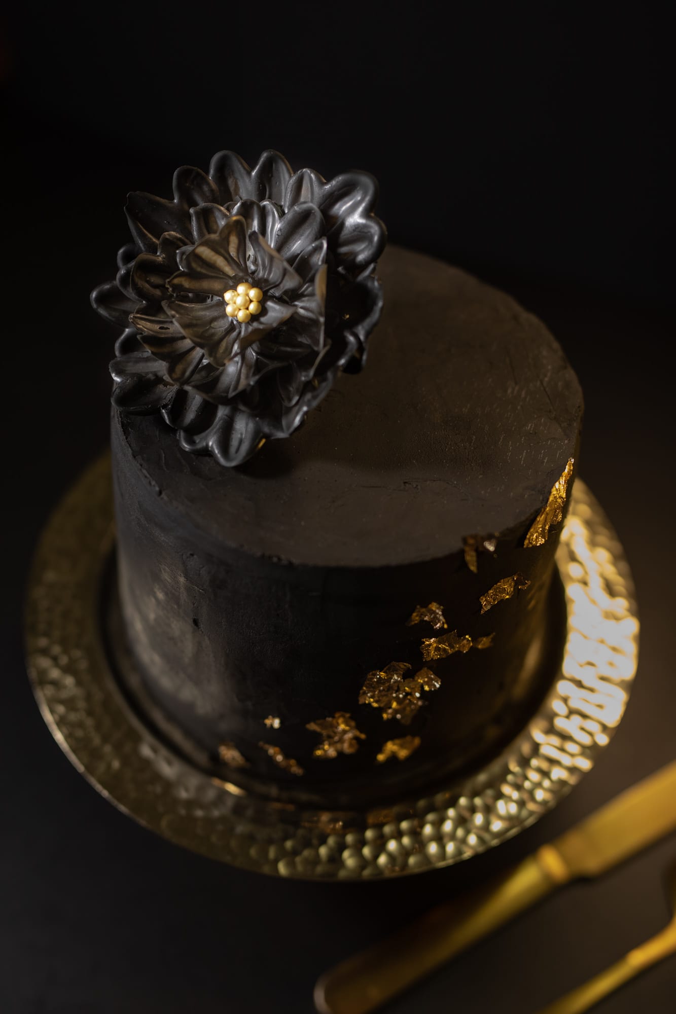 A black velvet cake topped with a dark chocolate flower on a hammered gold plate
