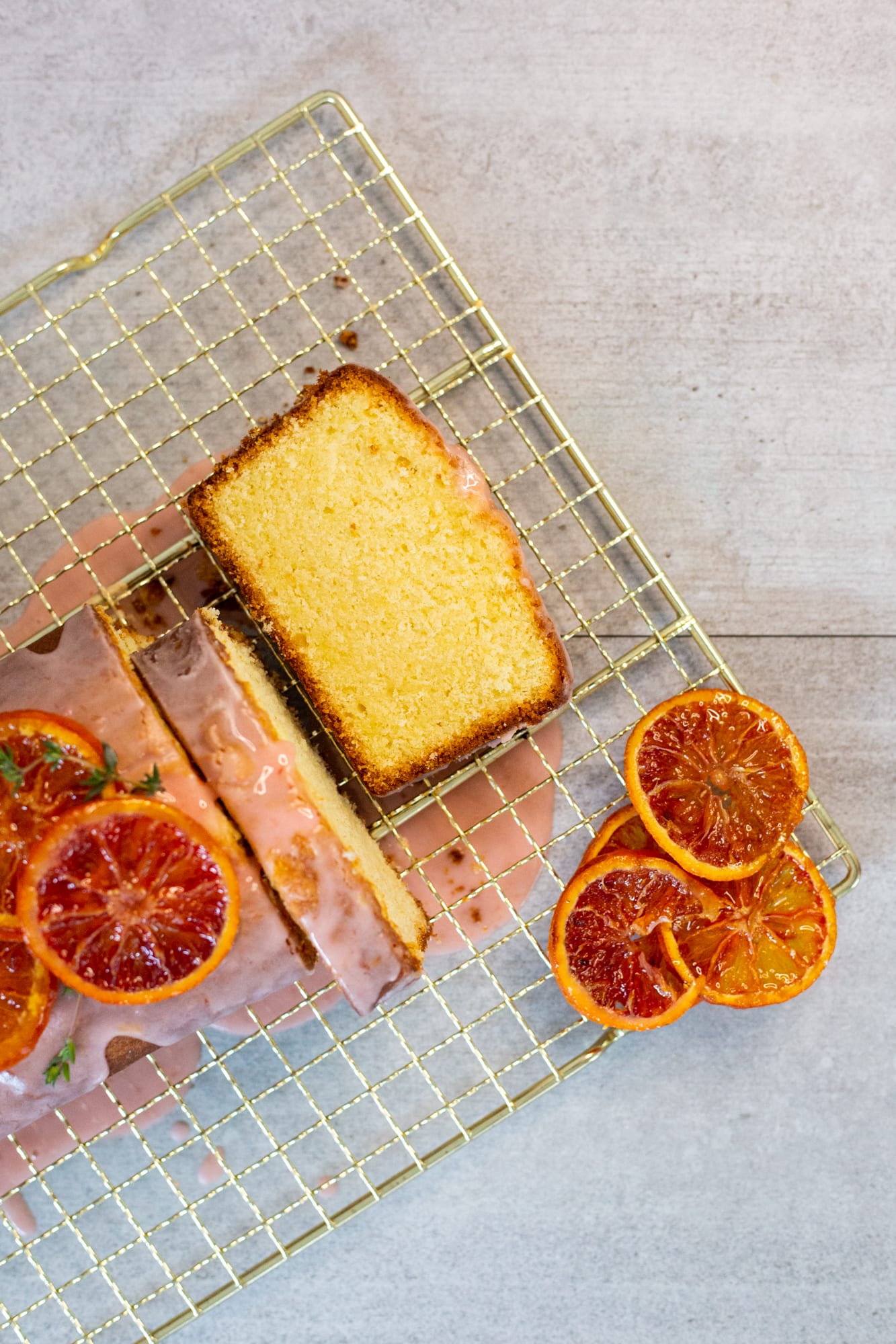 A sliced cream cheese pound cake on its rack with blood orange slices, from above