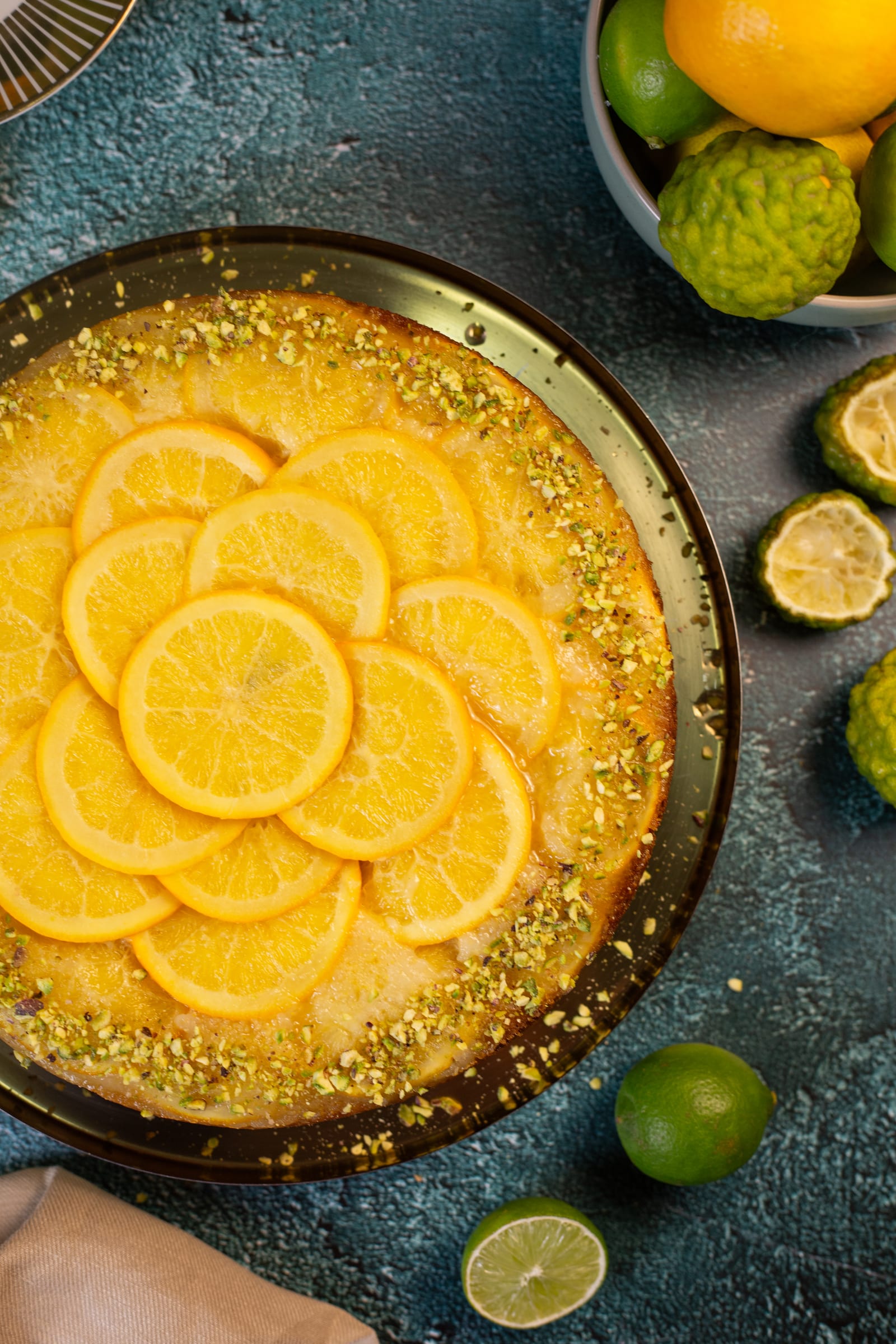 The orange and olive oil upside down cake from above, surrounded by limes and orange halves