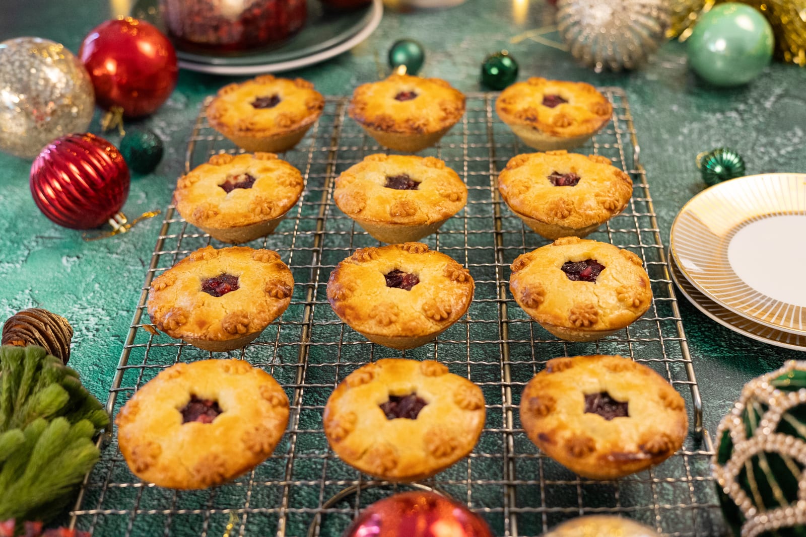 Rows of cherry and amaretto pies with star cut-outs on a wire rack, with Christmas baubles
