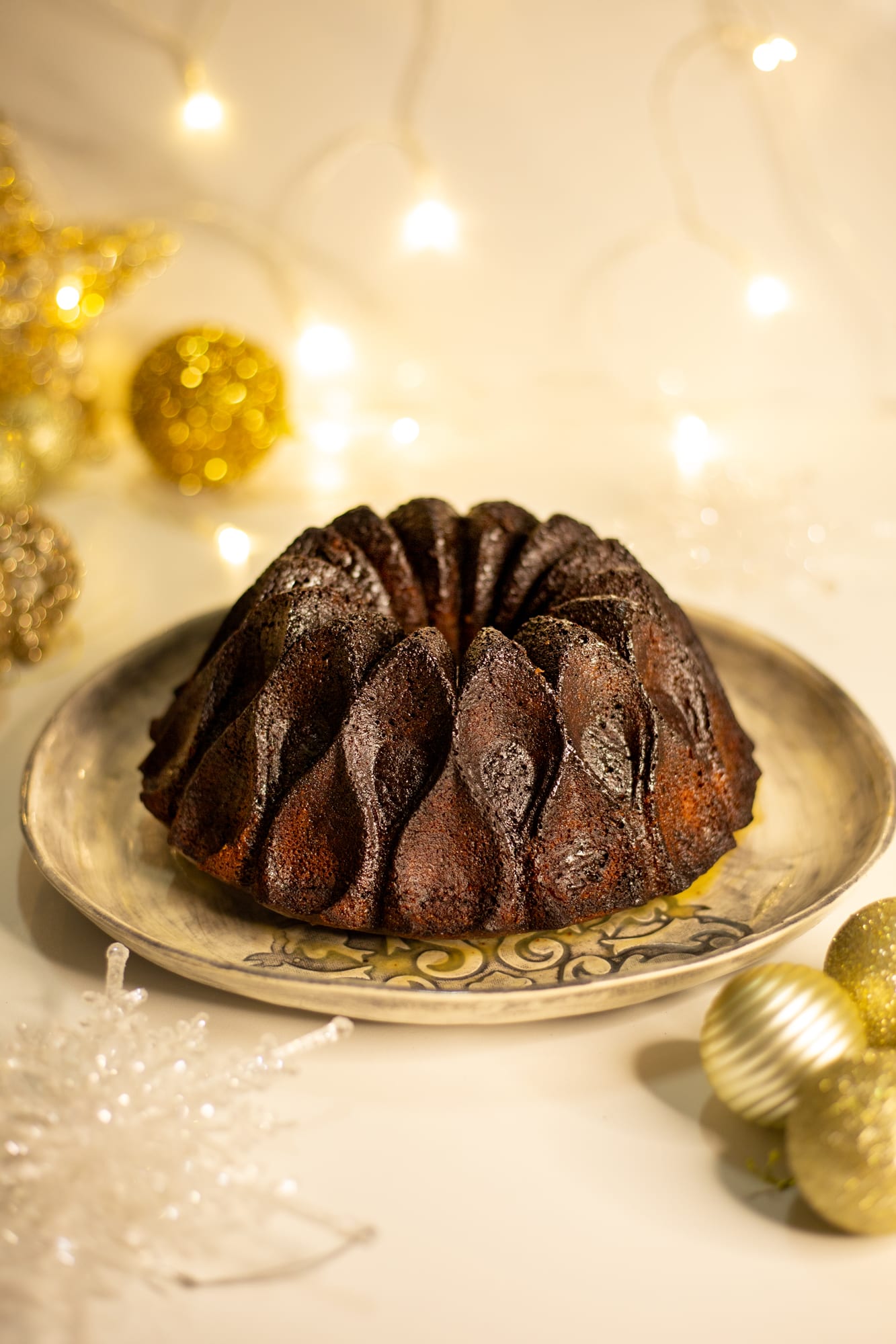 A gingerbread pudding baked in a bundt shape, on a plate with gold baubles