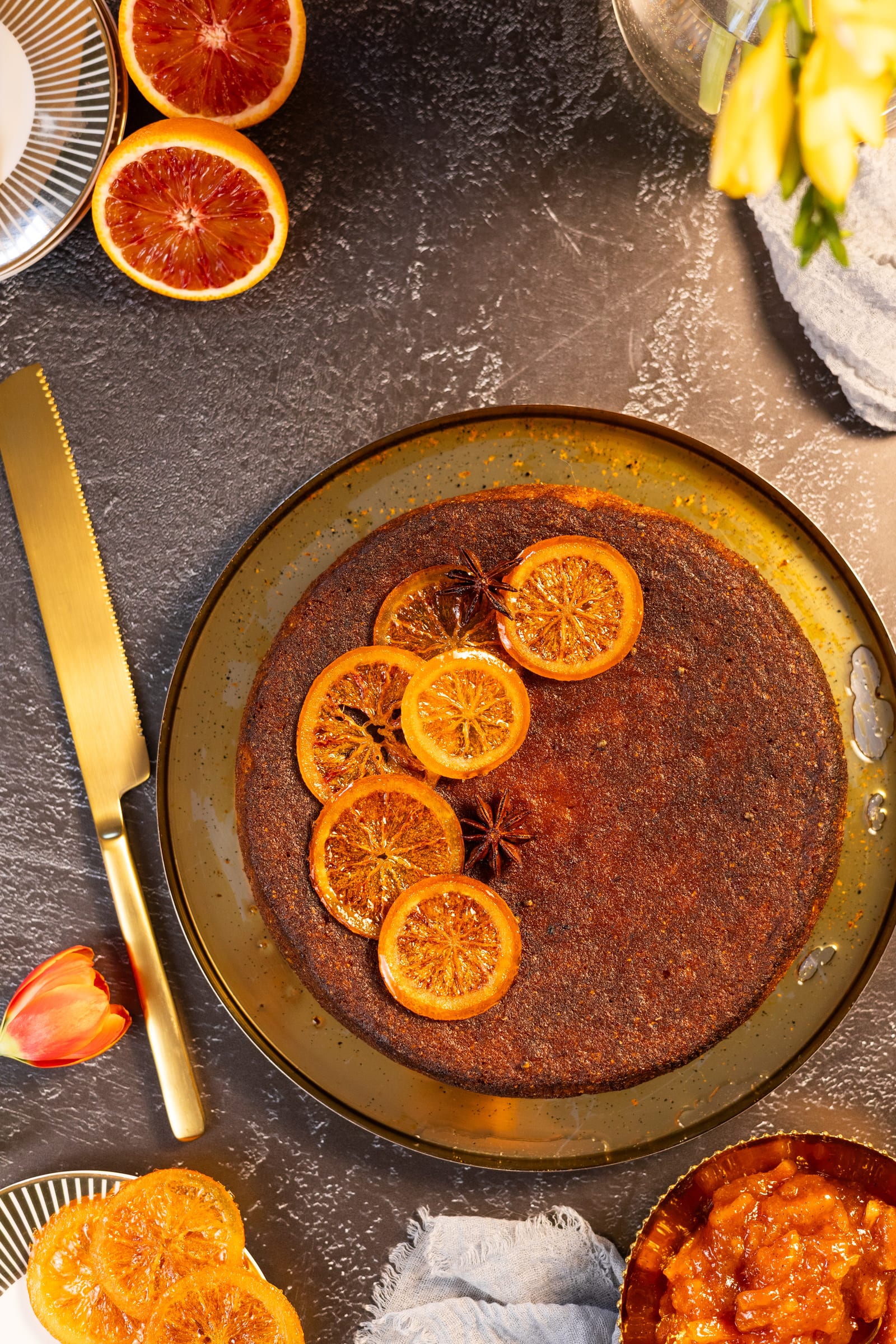 The polenta cake on a gold plate, from above, with blood oranges and a cake knife