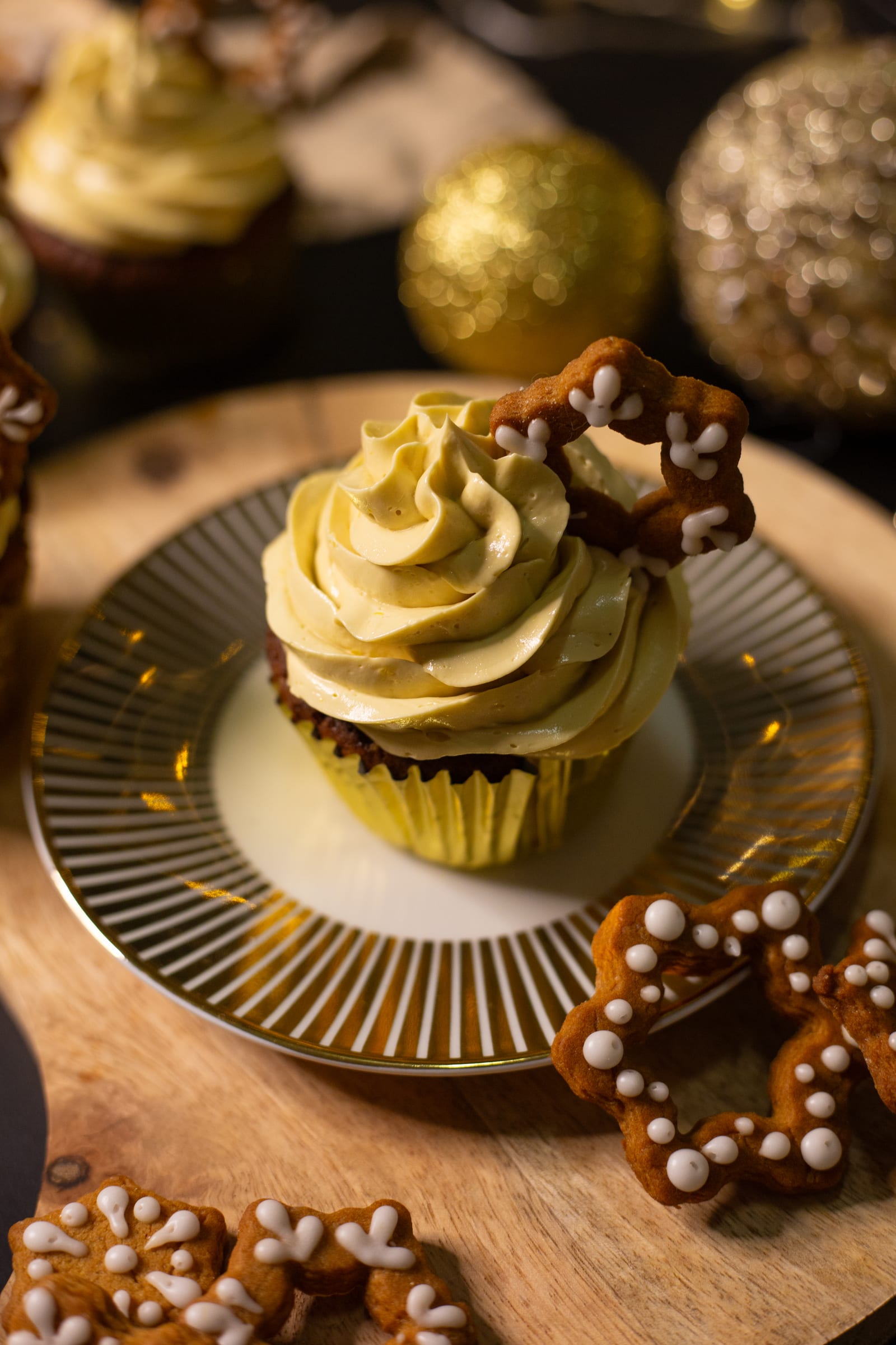A gingerbread cupcake topped with eggnog buttercream on a gold-striped plate, pretzel stars alongside