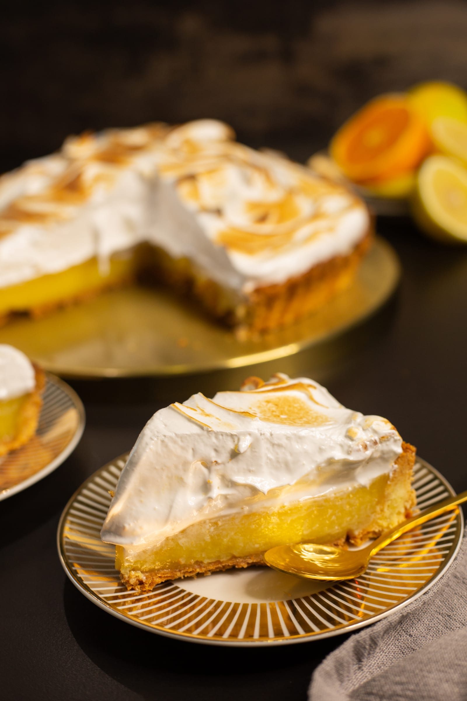 A slice of lemon meringue pie on a plate in front of the cut pie