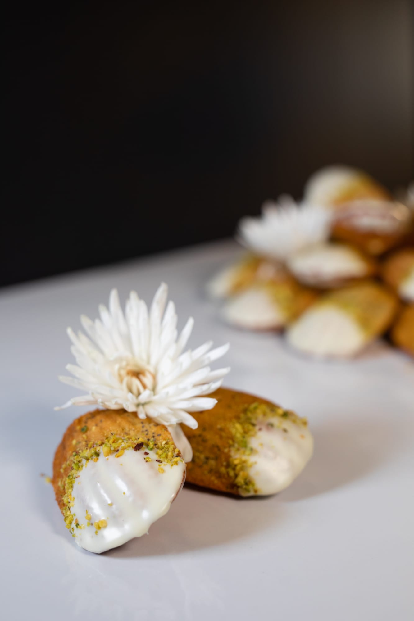 A single lemon and poppyseed madeleine dipped in white chocolate and pistachio, with a flower