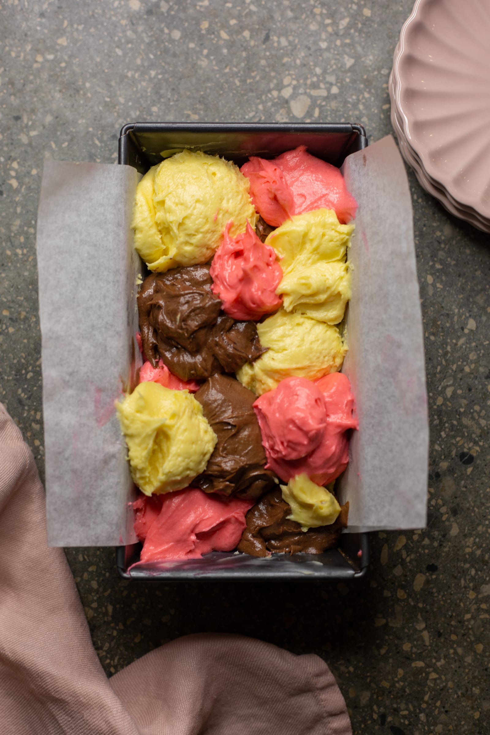 Dollops of vanilla, strawberry and chocolate batter in a lined loaf tin