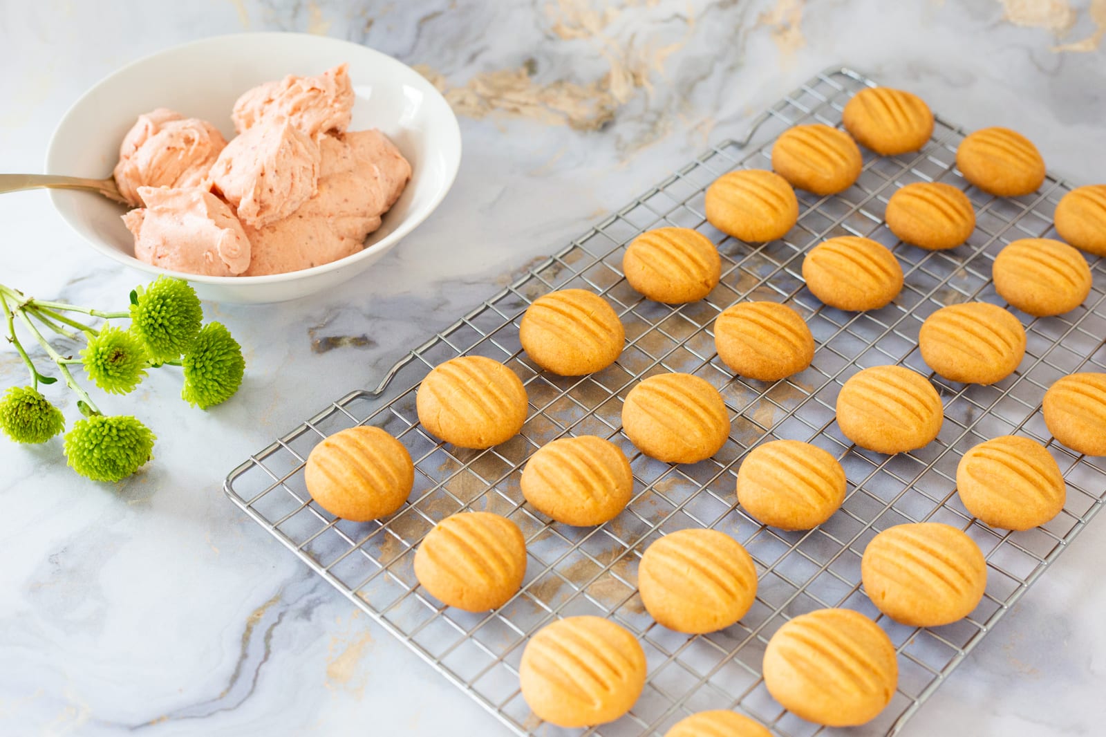 Rows of plain custard biscuits on a wire rack beside a bowl of pink filling, from above