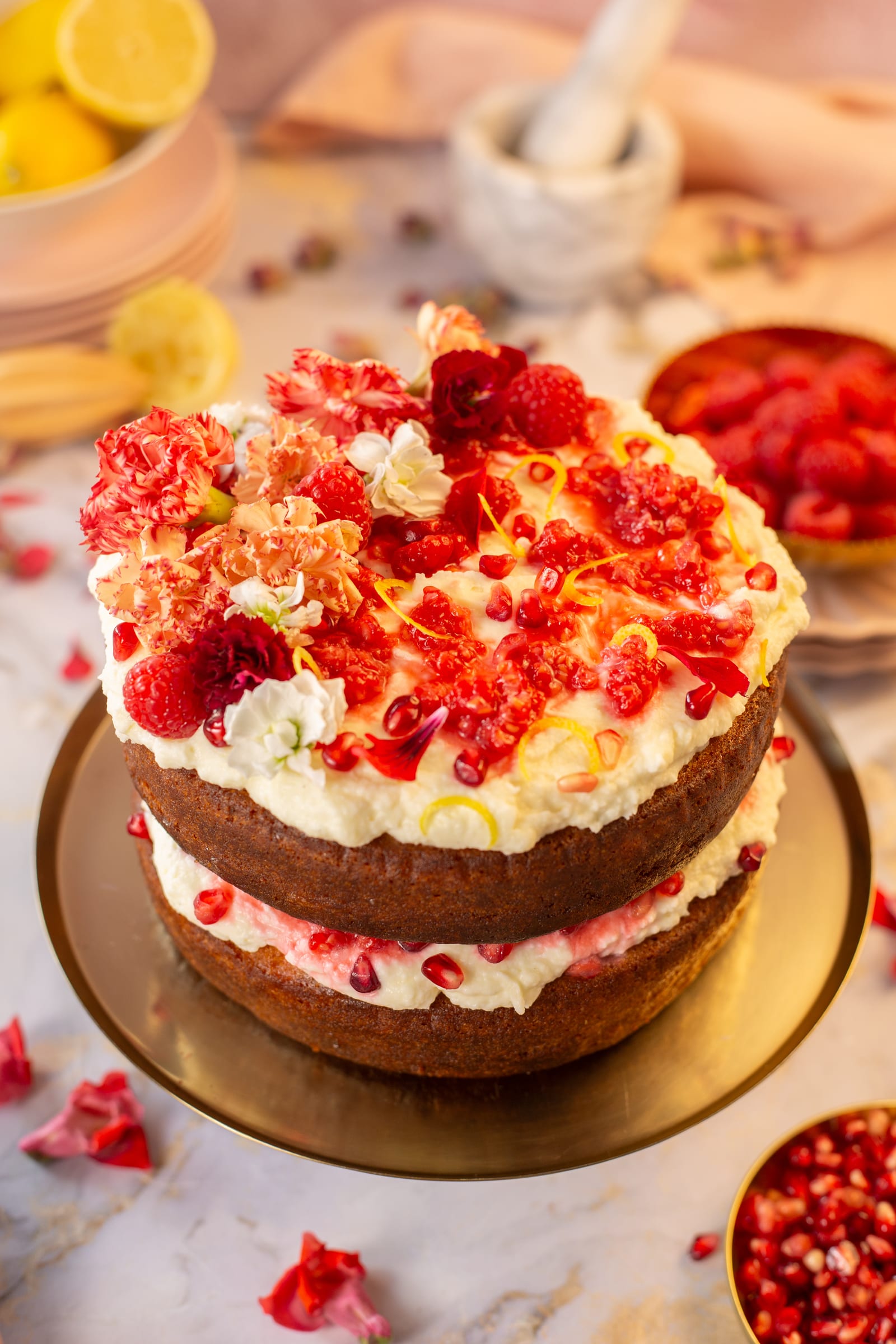 The layered cake on a gold stand, with lemons and raspberries behind