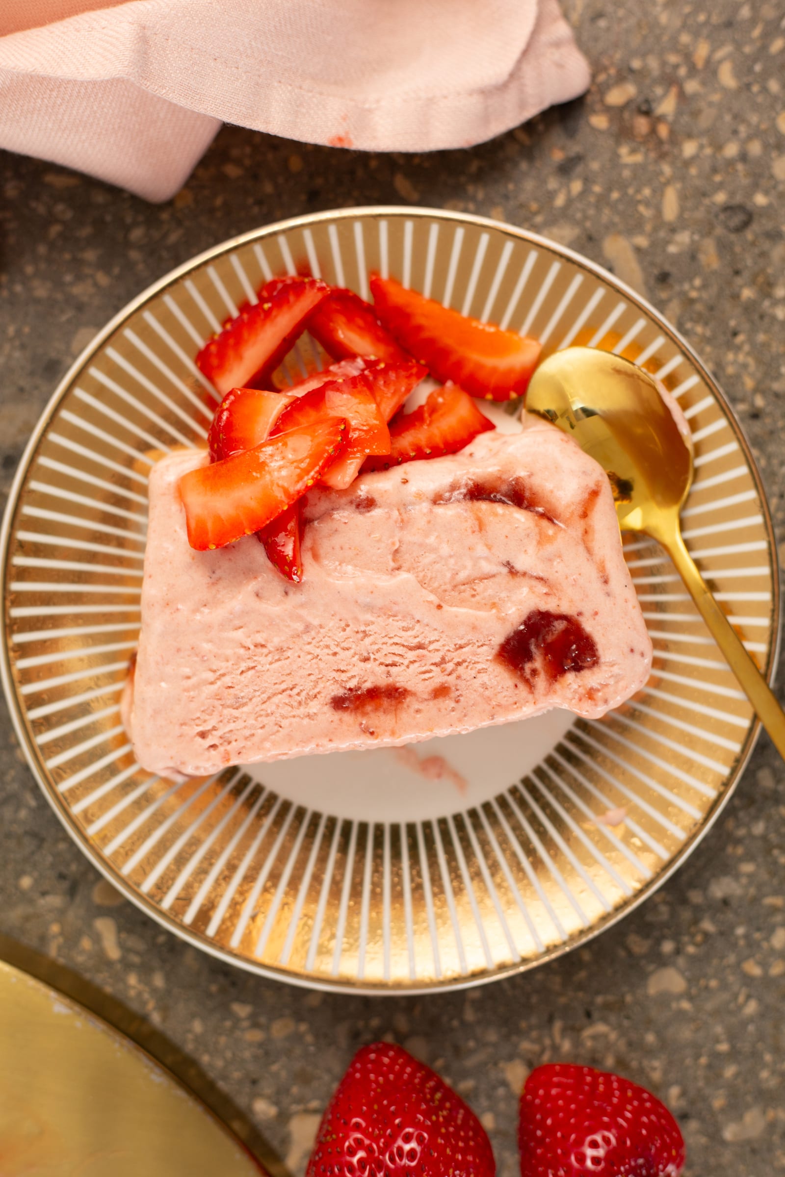A slice of roasted strawberry and rosemary semifreddo from above with a gold spoon and fresh strawberries