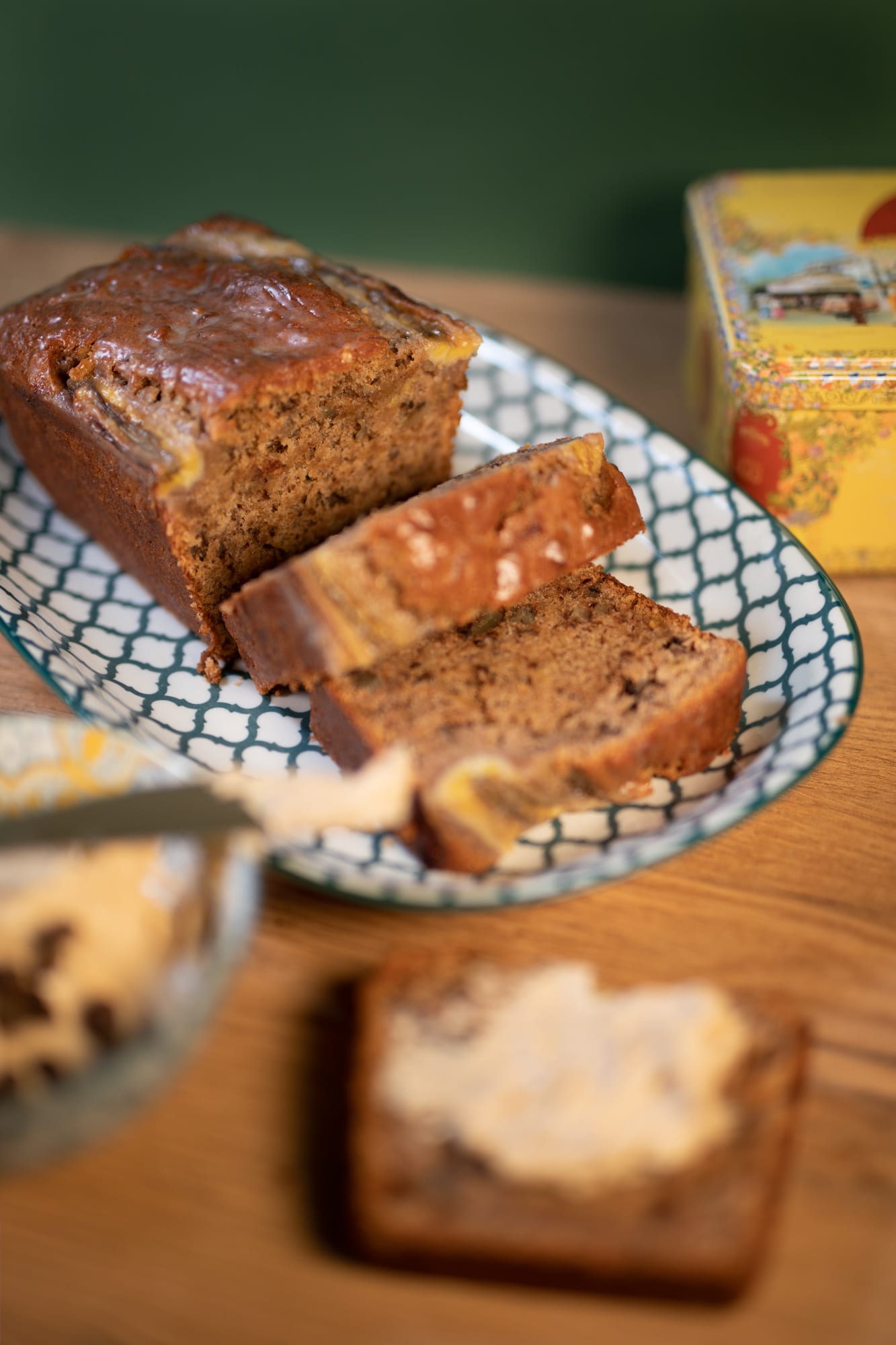 A sliced banana and pecan nut bread on a blue and white dish, a buttered slice blurred in front
