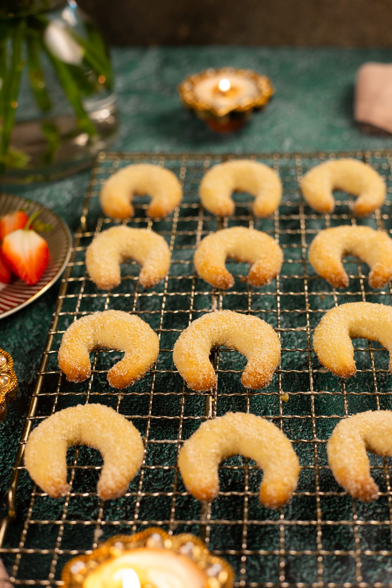 Cashew nut biscuit crescents on a wire rack, with a lit diya