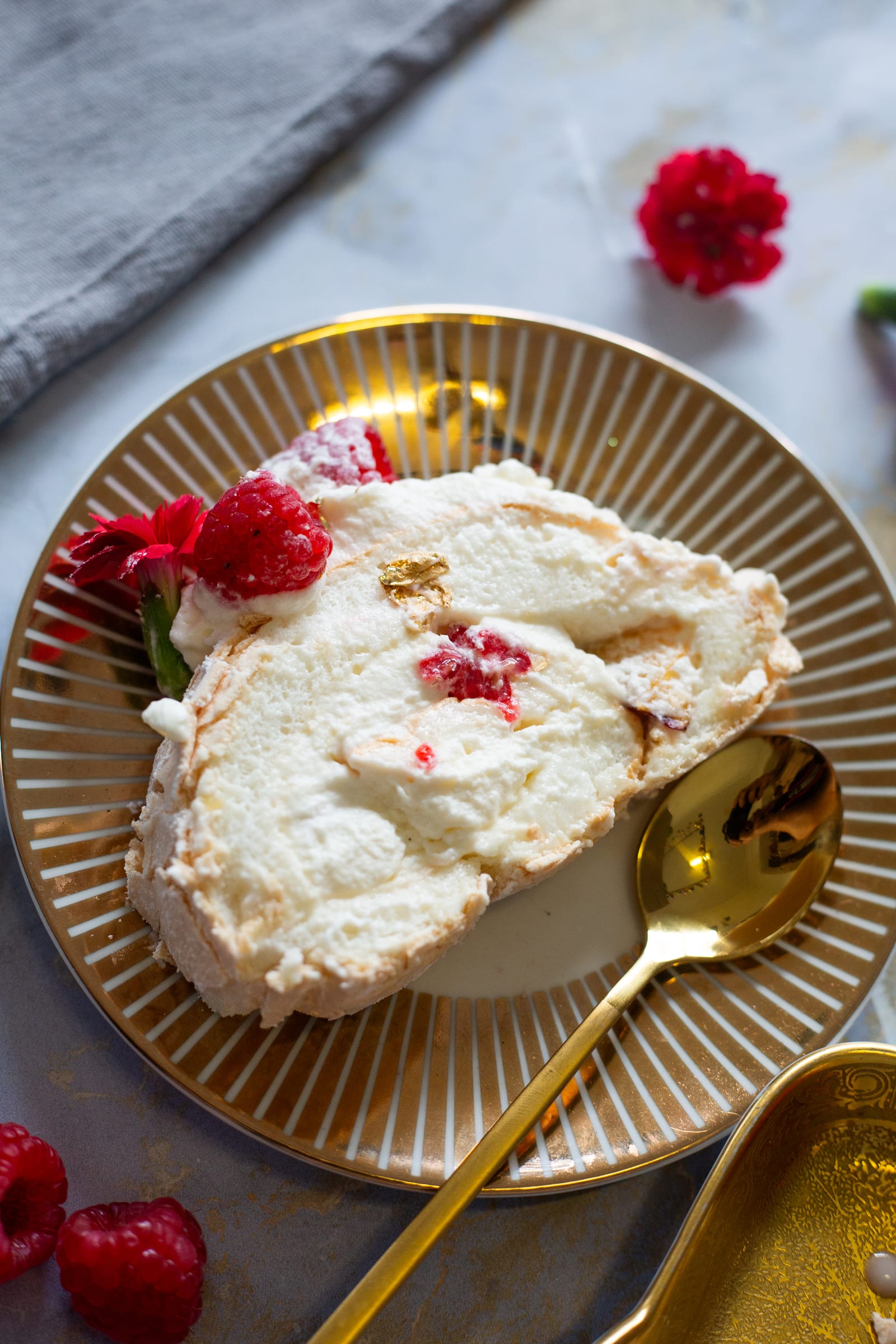 A slice of raspberry and nectarine pavlova roulade on a striped gold plate, showing the cream spiral