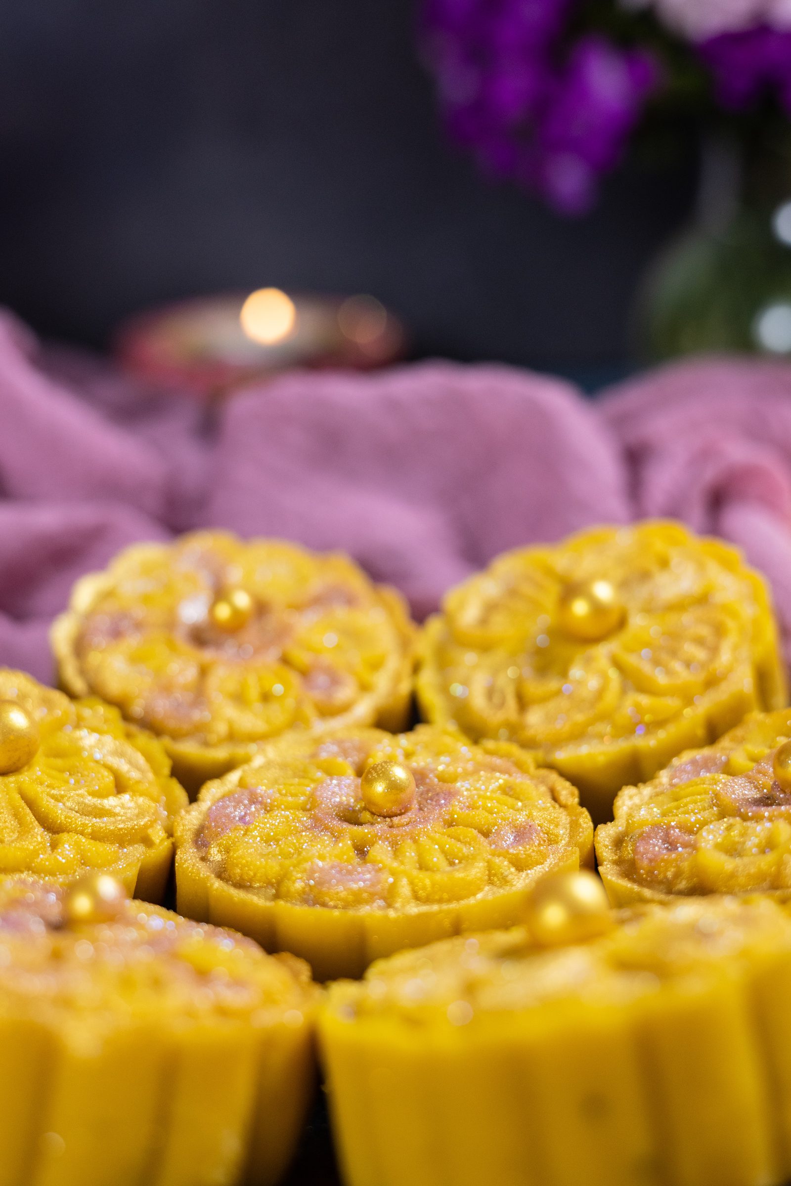 Close-up of flower-shaped mango burfee from the side, with a candle glowing behind