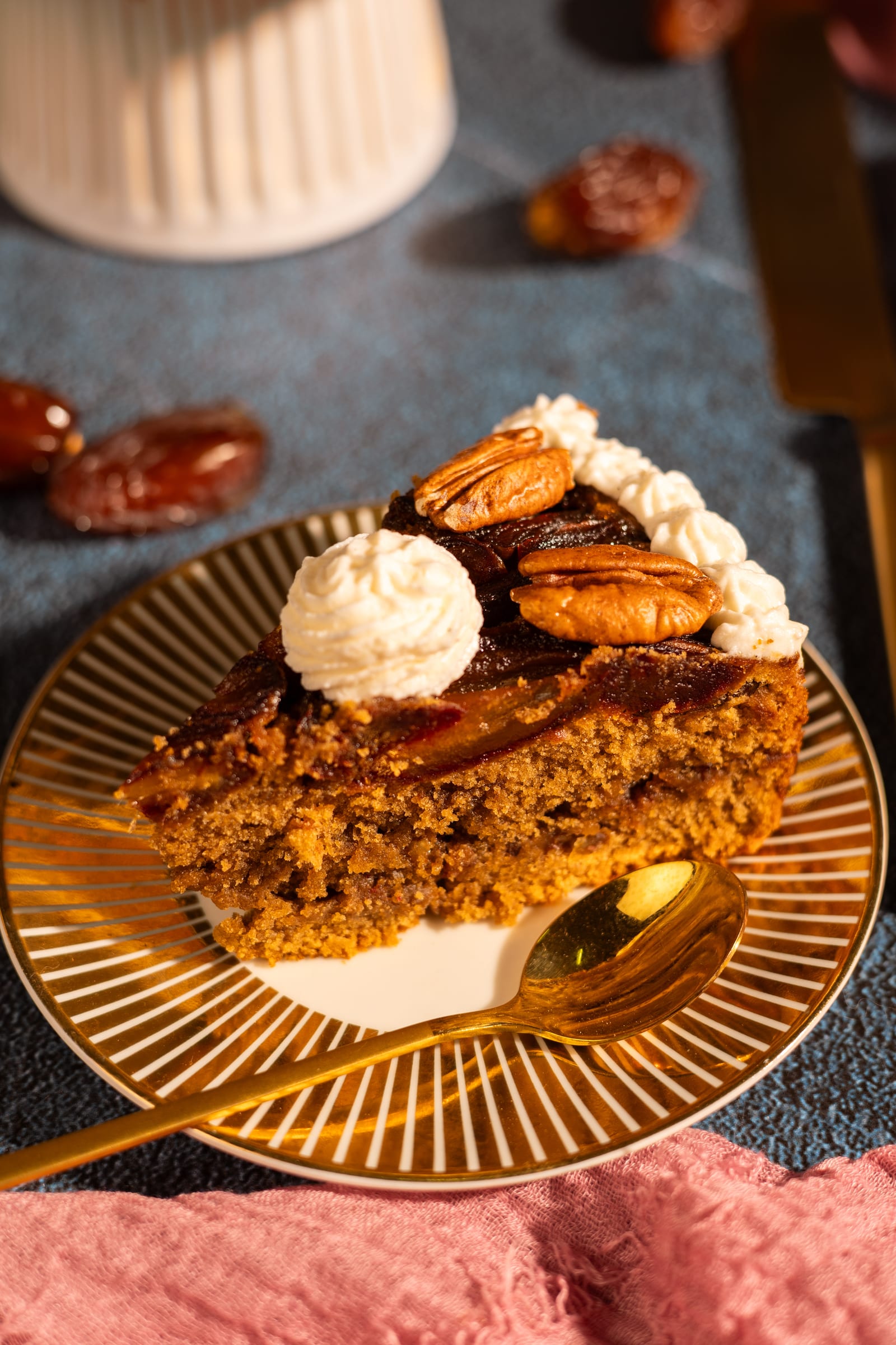 A slice of date and pecan cake with cream on a gold plate