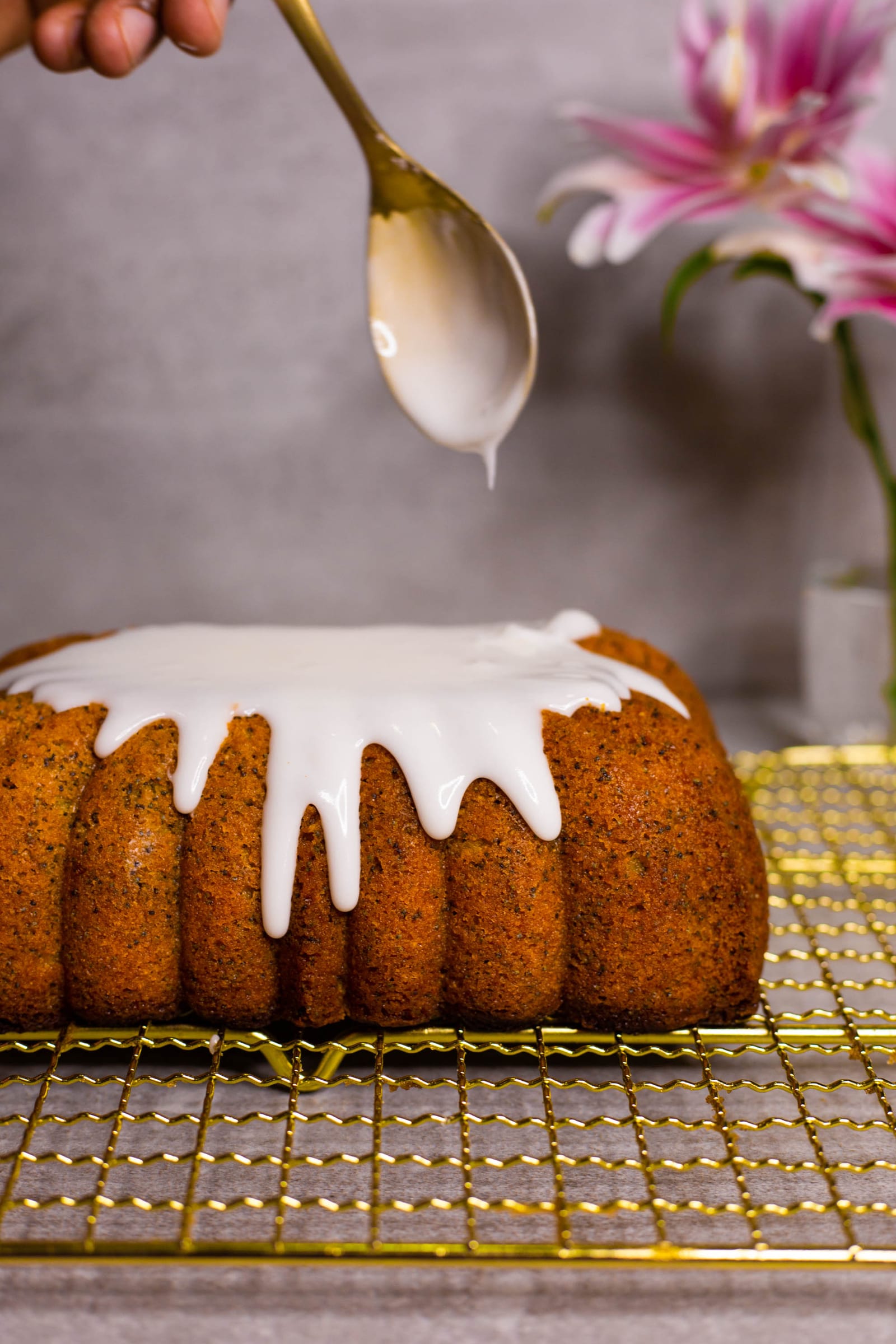 Lemon glaze dripping from a spoon down the sides of a gluten-free lemon and poppyseed loaf