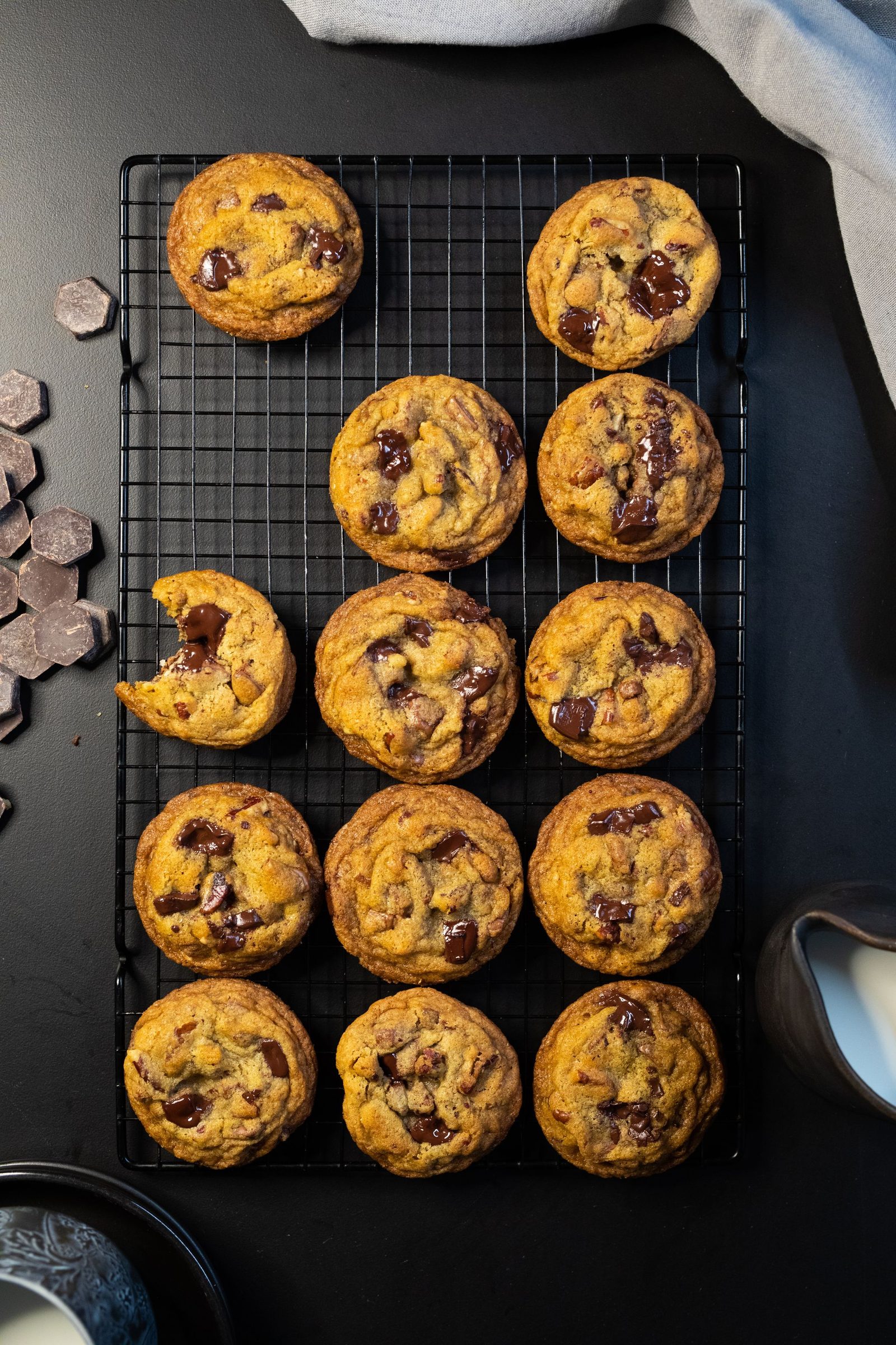 A cooling rack full of chocolate chip cookies with chocolate chunks and a glass of milk, from above