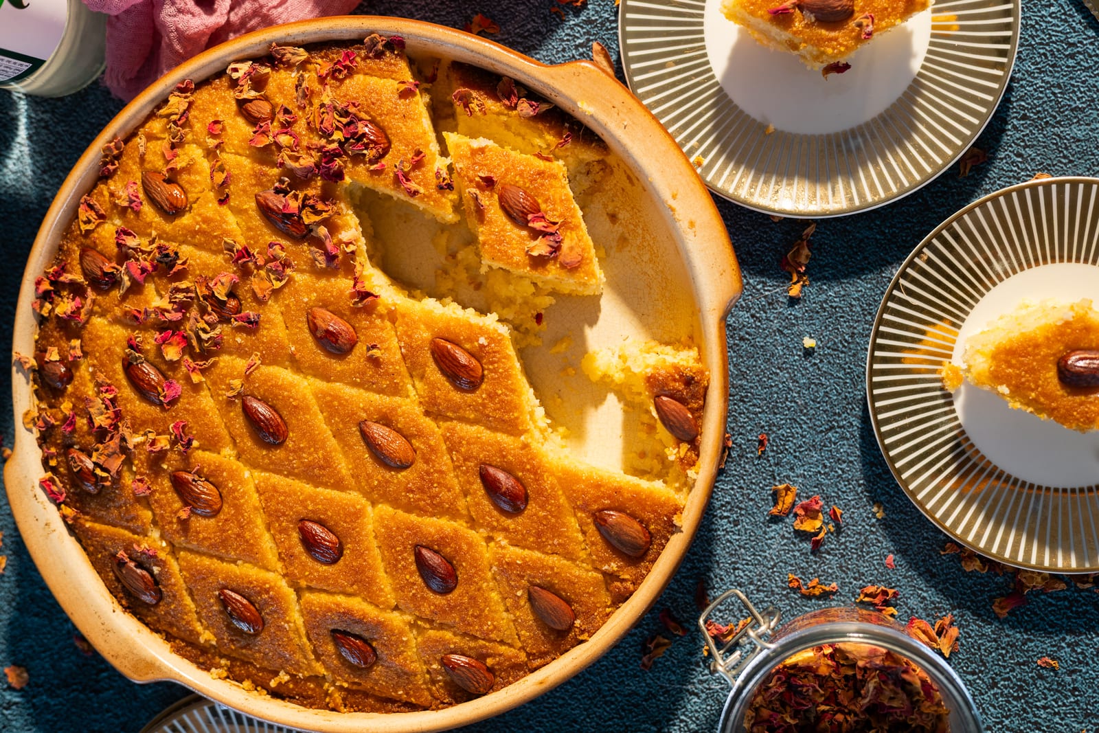 The basbousa with a piece cut out, beside a cup of cream