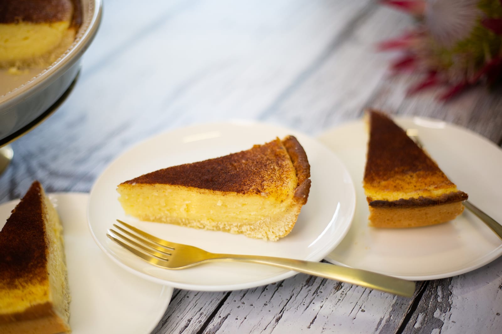 Slices of melktert on white plates with gold forks and proteas