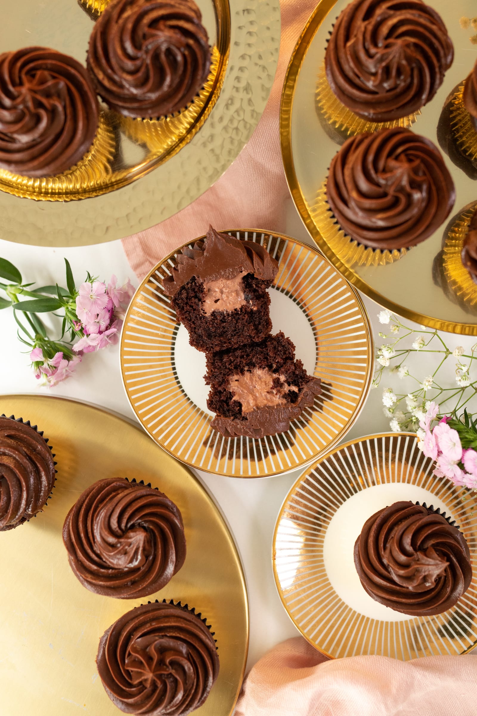 Ultimate triple chocolate cupcakes on gold plates, one halved to show the mousse filling, from above
