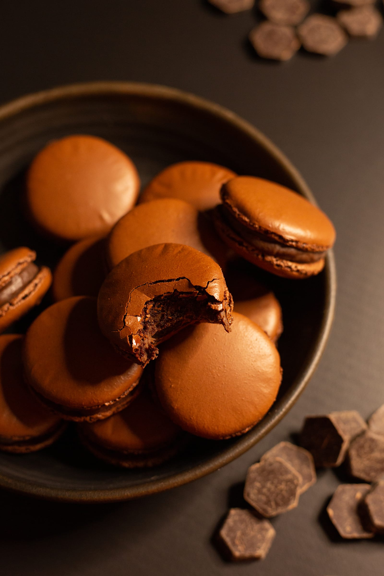 Looking down into a bowl of chocolate macarons, one with a bite taken