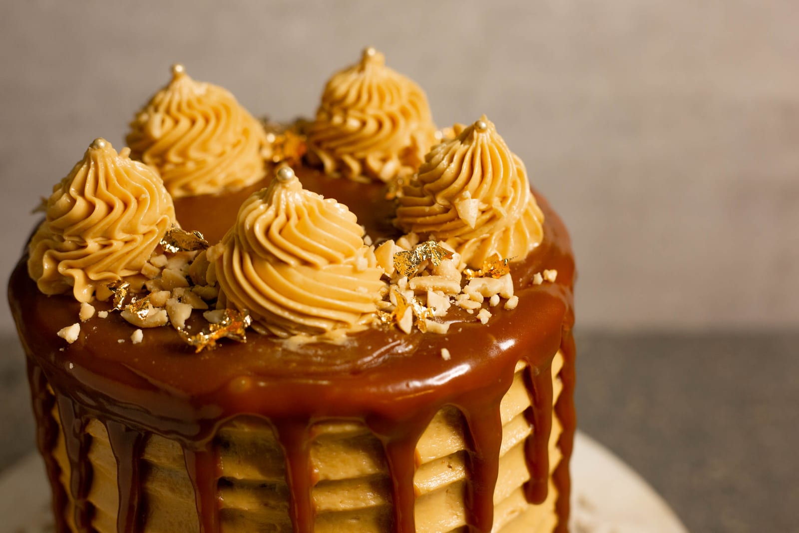 Close-up of the piped rosettes and caramel drip on a salted caramel peanut cake, from the side