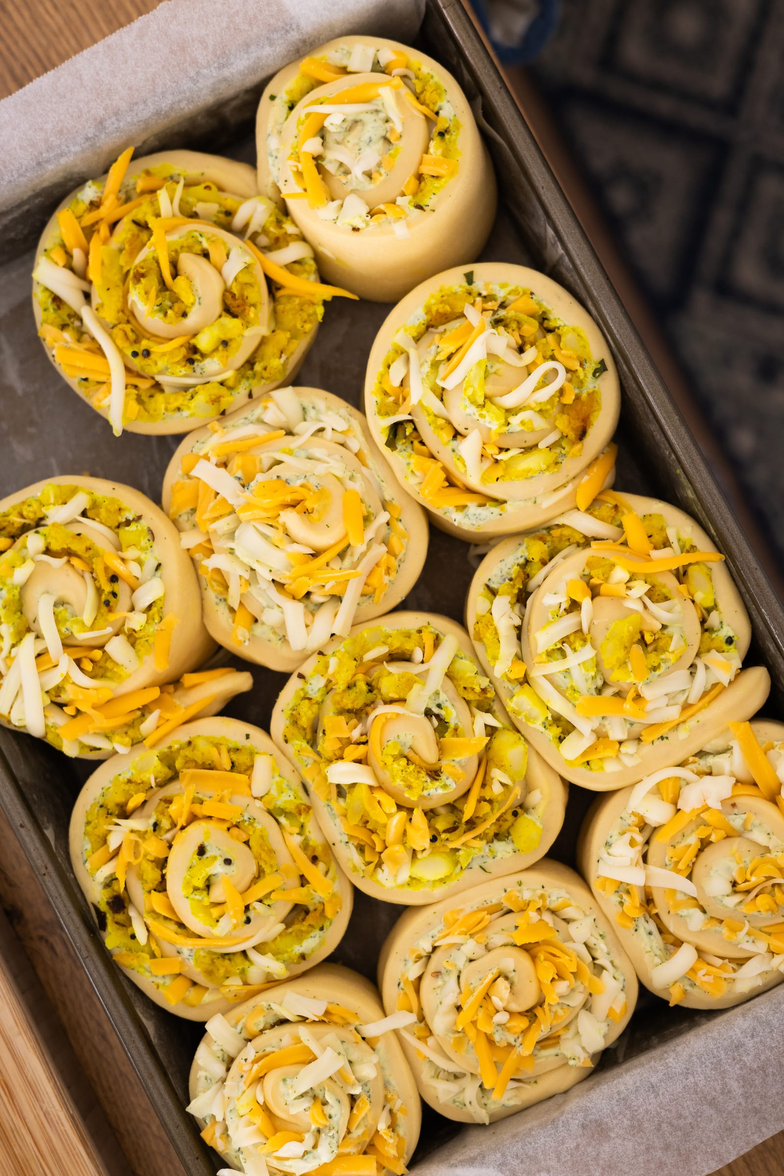 Unbaked scrolls filled with potato and cheese, rising in a lined tray