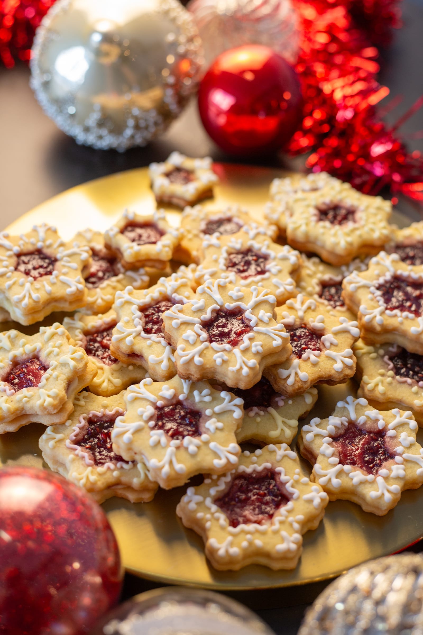 Star-shaped lemon and raspberry Linzer cookies heaped on a gold platter among red and silver baubles