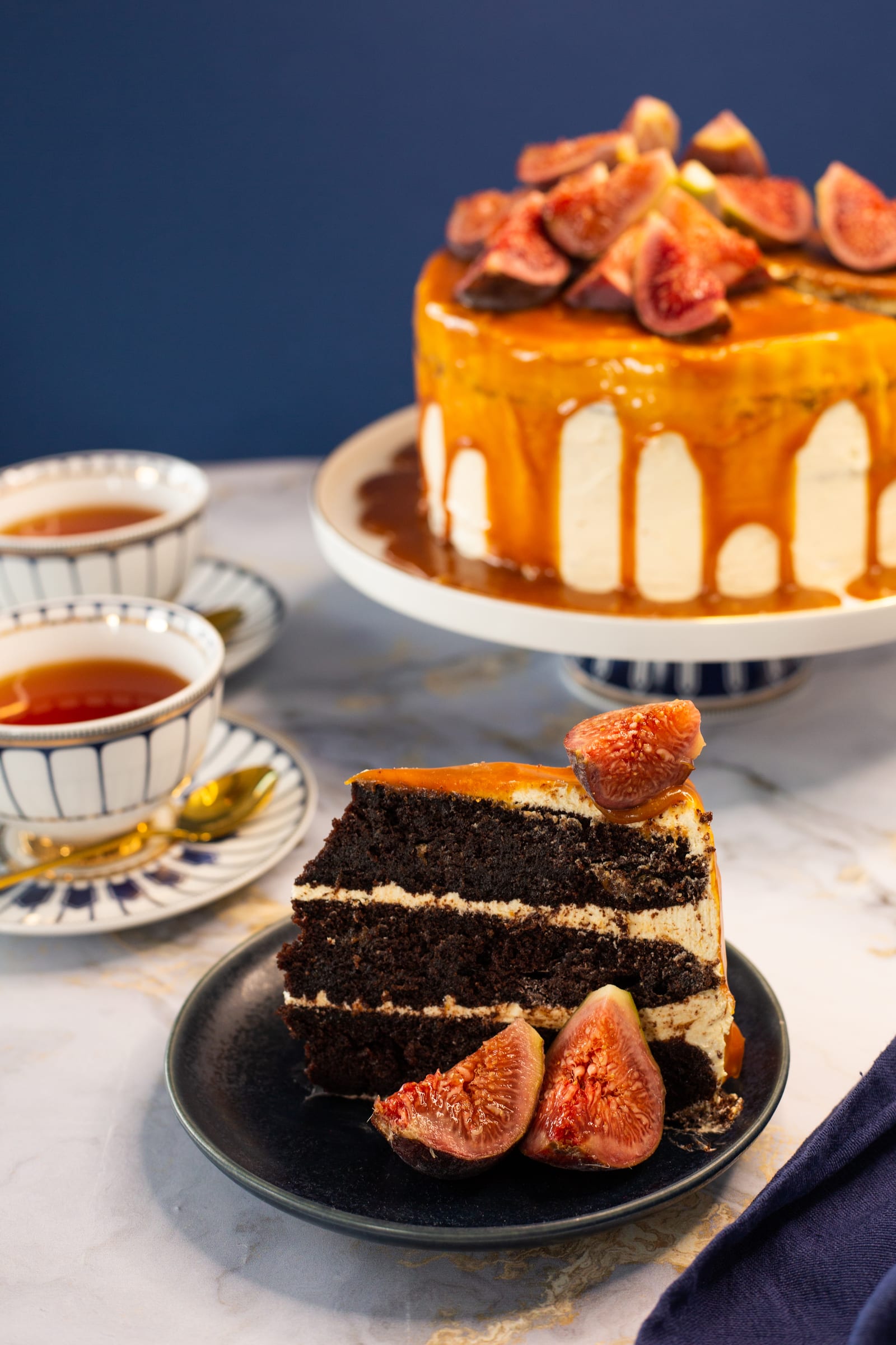 A slice of devil's food cake with hazelnut buttercream and a fig on a navy plate