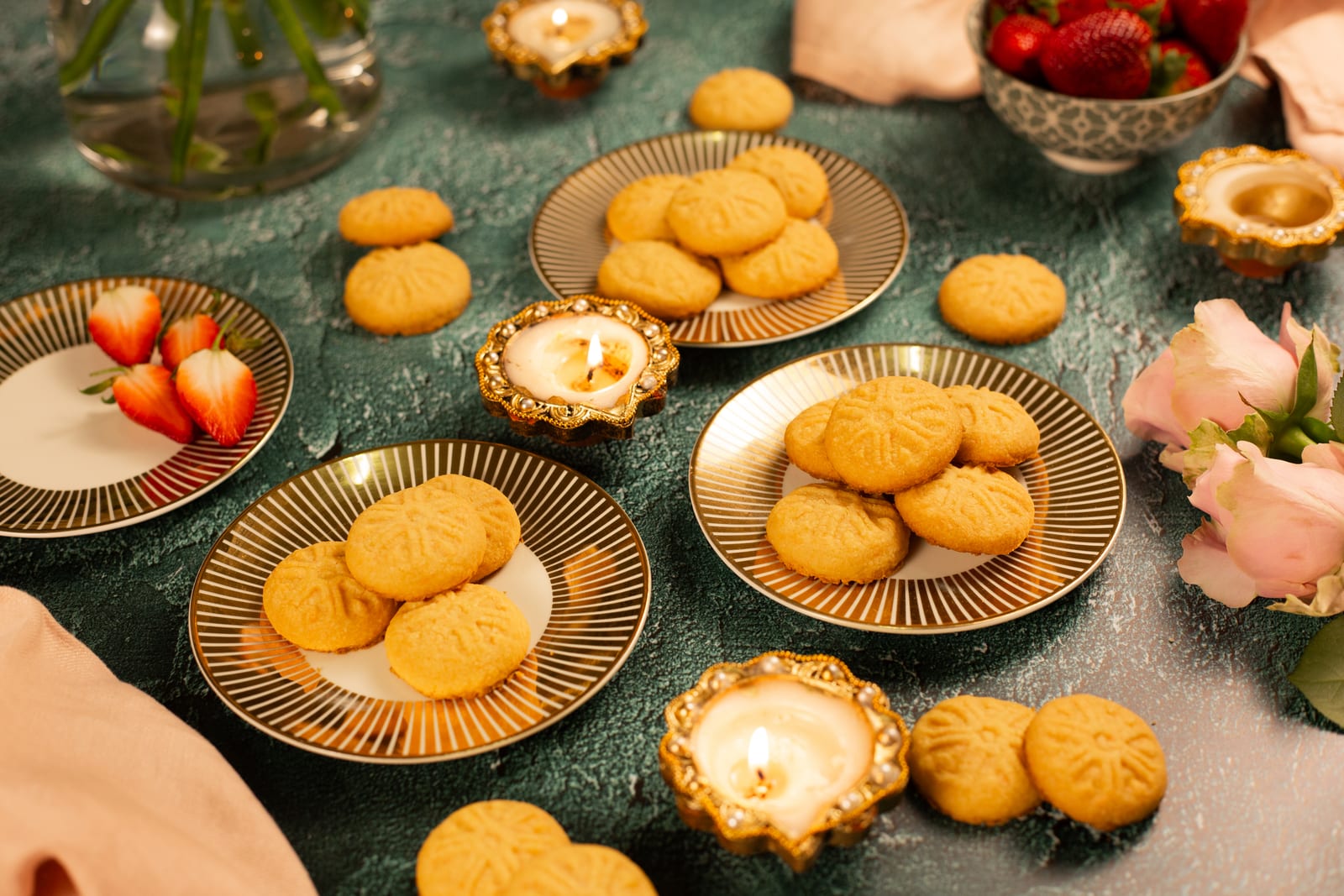 Custard biscuits on gold plates, with lit diyas, strawberries and roses