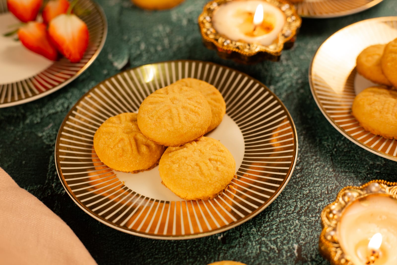 Close-up of custard biscuits with their pressed pattern, beside strawberries and a diya