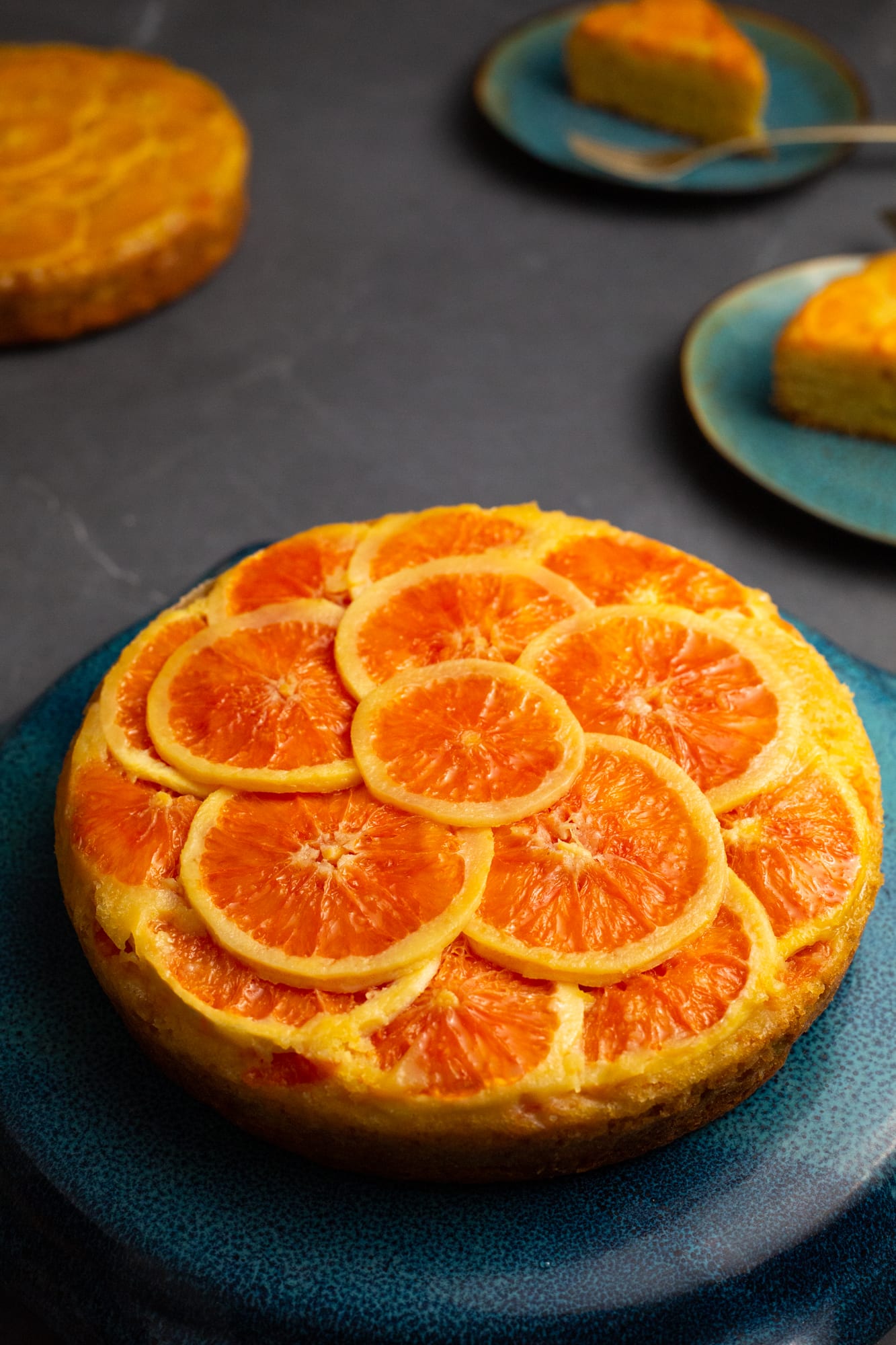 A whole orange upside down cake on a teal plate, another cake behind