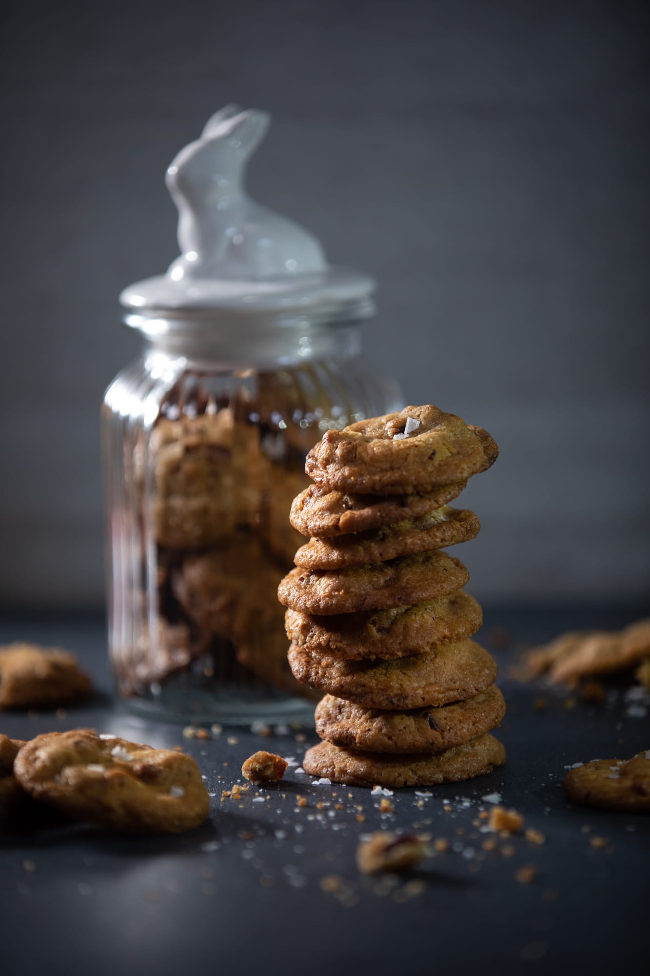 A tall stack of pecan and white chocolate salted cookies in front of a jar with a bunny lid