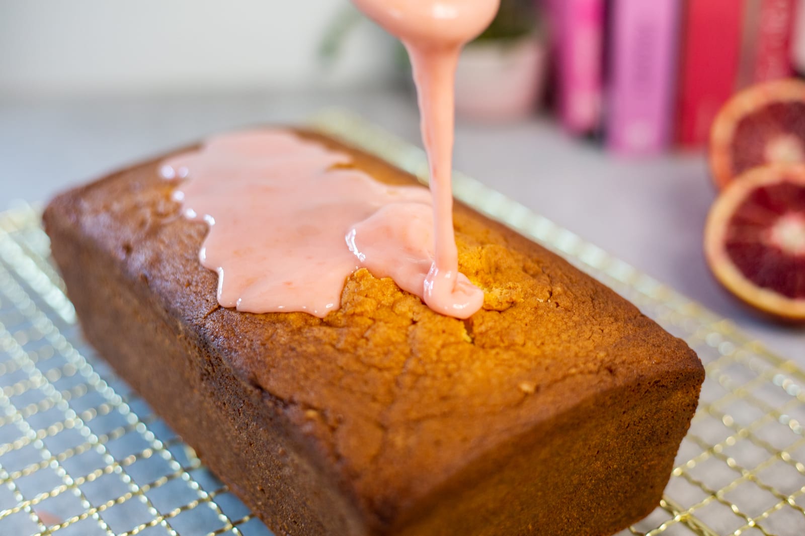 Blood orange glaze being poured from a spoon over a cream cheese pound cake