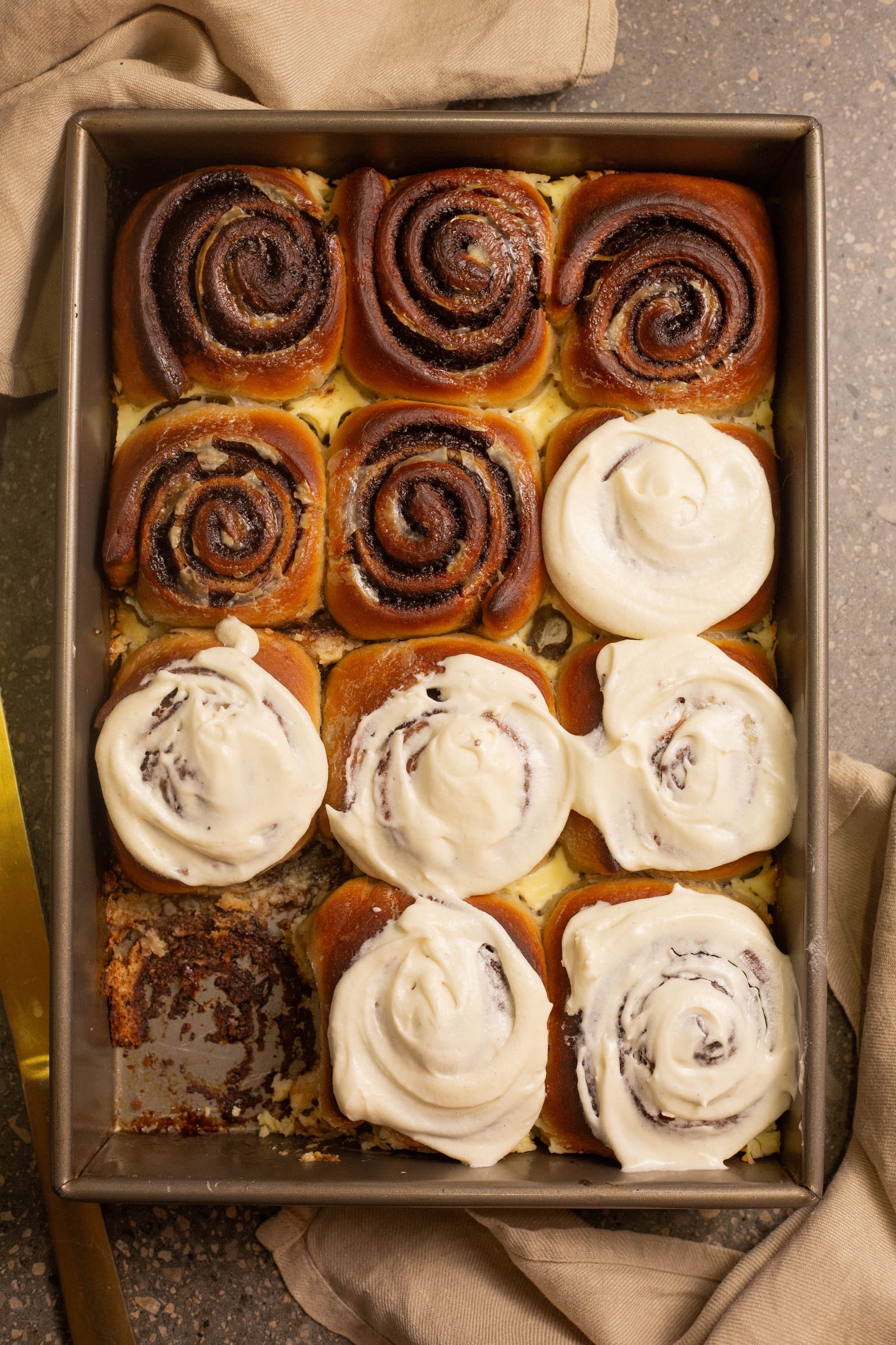 A tin of cinnamon rolls, half iced with cream cheese icing, from above