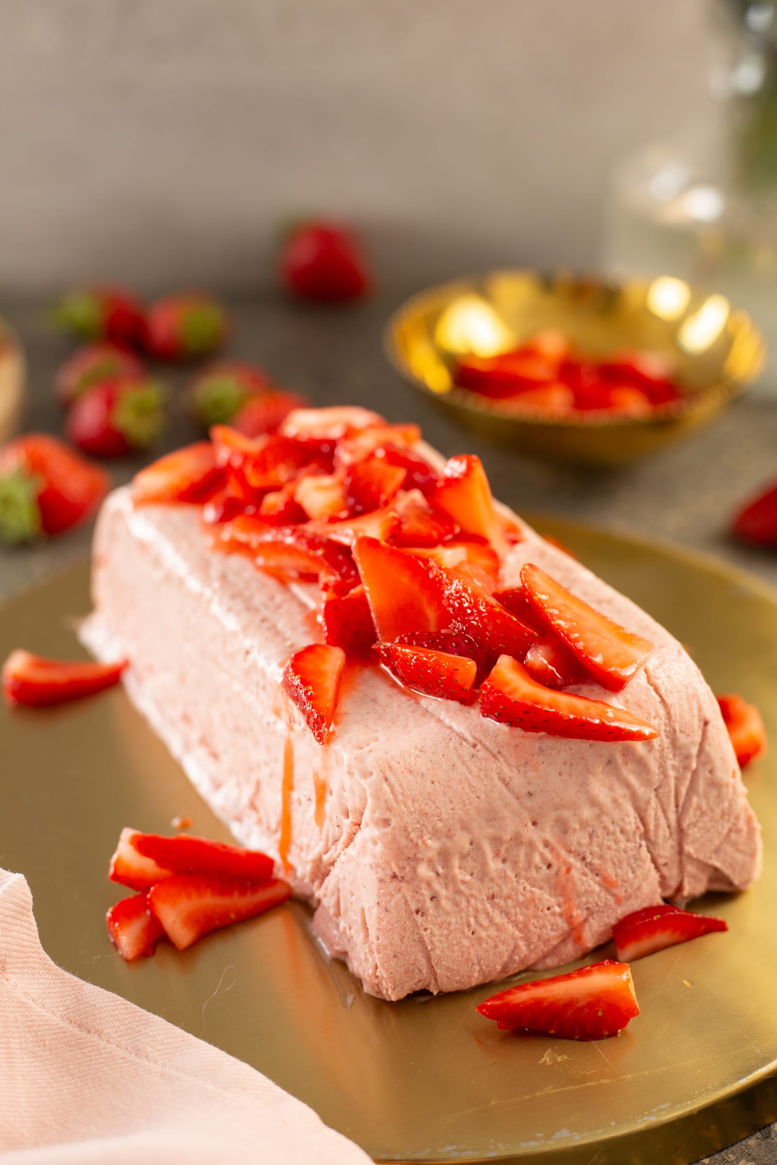 A whole roasted strawberry and rosemary semifreddo topped with roasted strawberries on a gold plate