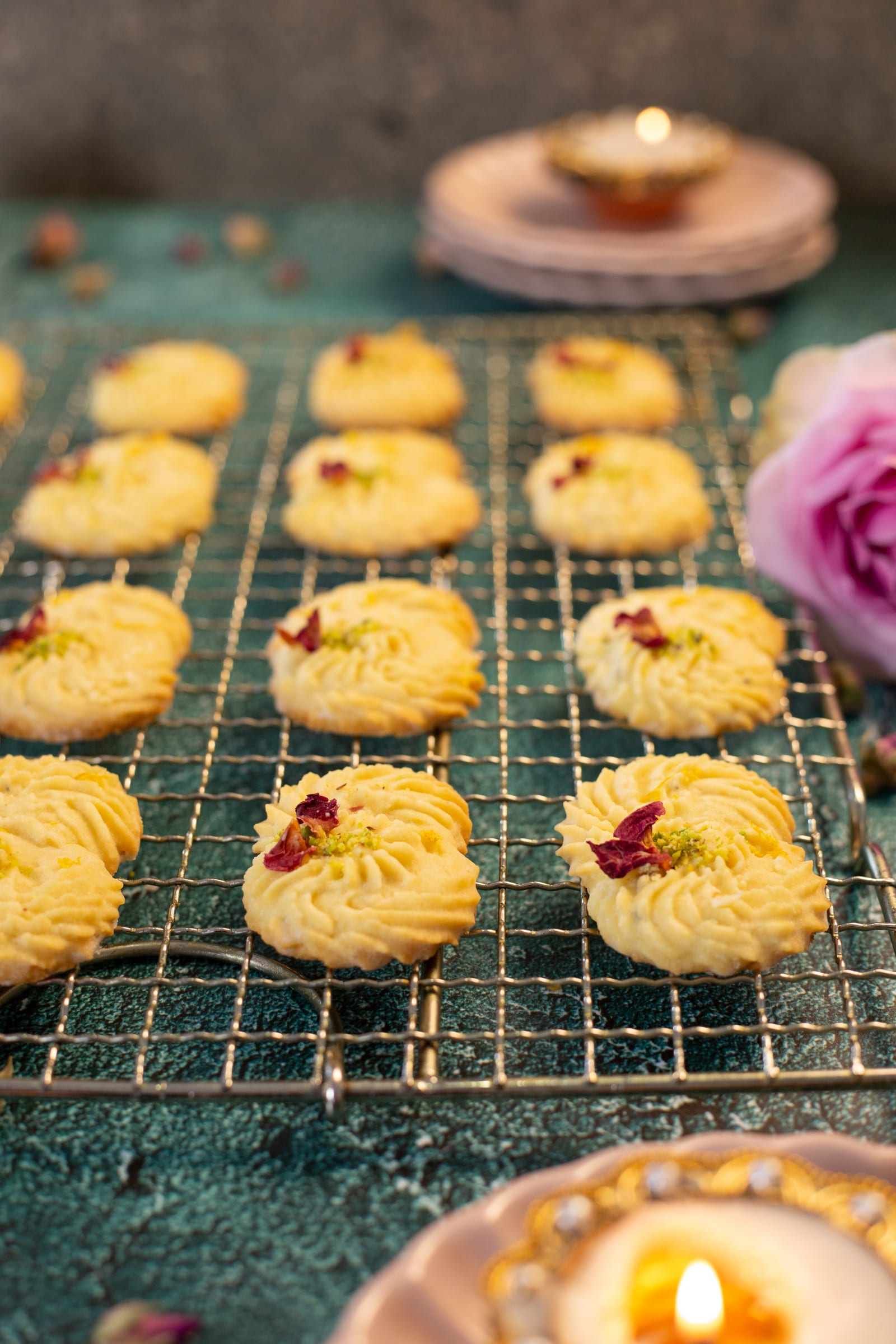 Piped biscuits on a rack, with a lit diya and pink roses